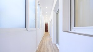 Um corredor estreito e bem iluminado, com soalho de madeira e grandes janelas em ambos os lados.