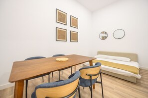 Una stanza con un tavolo di legno, quattro sedie, un letto e quattro quadri appesi al muro.