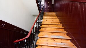 Uma escadaria de madeira com corrimão vermelho, ladeada por paredes de madeira escura e uma parede branca no topo.