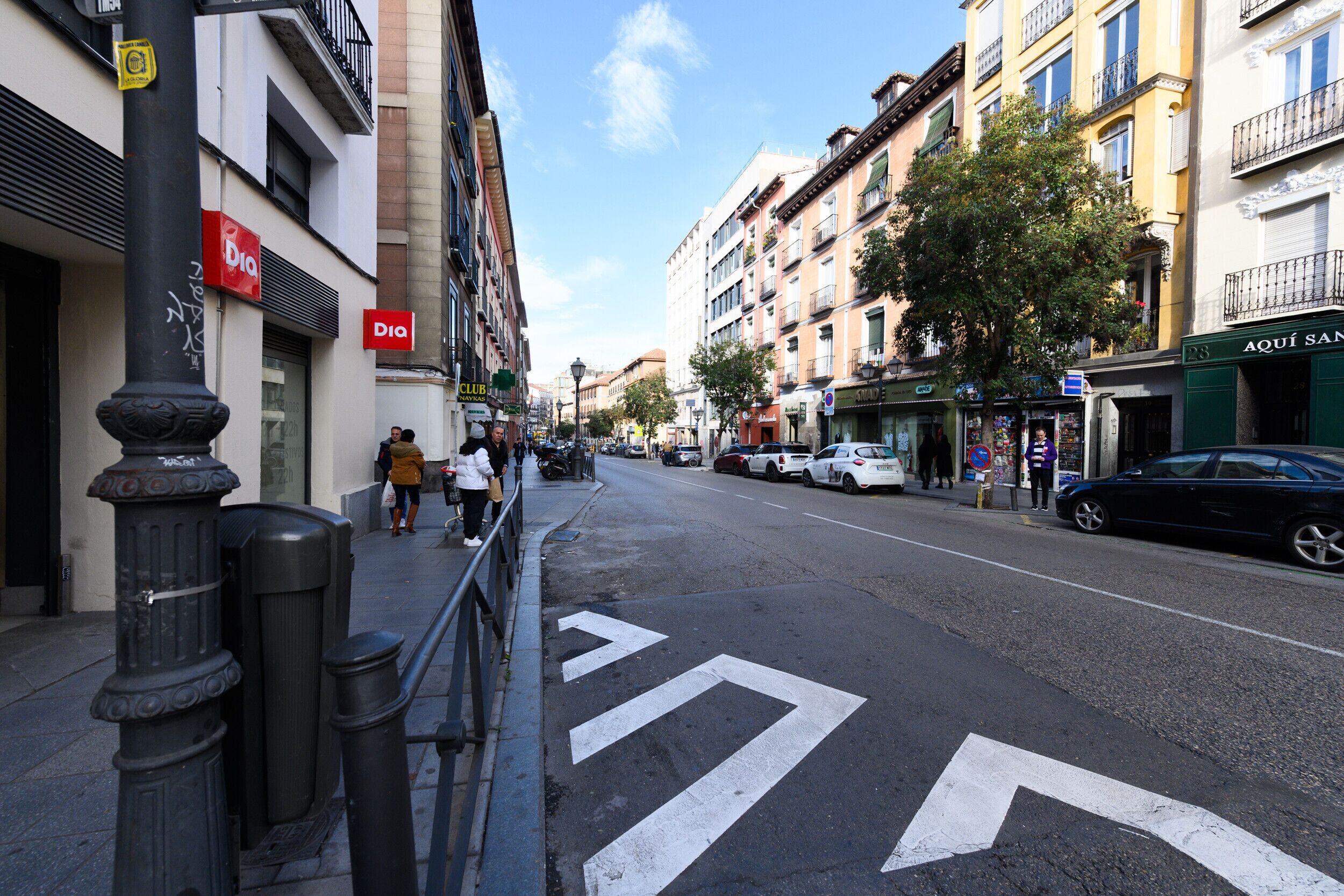 A street with buildings on both sides, a clear sky, and a pedestrian crossing.