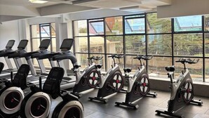 A gym with stationary bikes and treadmills, large windows, and a view of buildings outside. - Cosy apartment in KILIMANI 
Mini golf 
restaurant 
Smrt TV
parking 
gym
security (Nairobi)