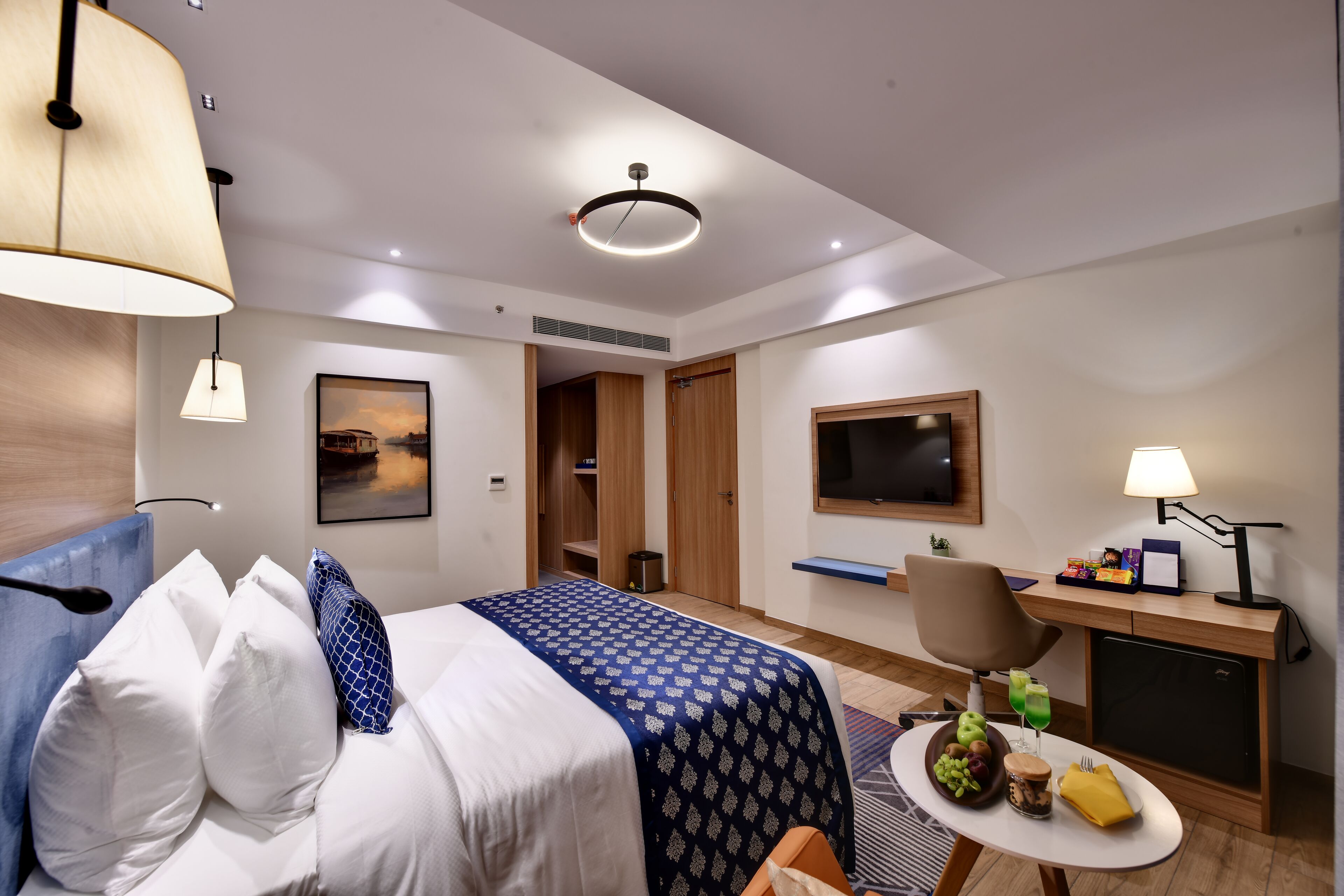 A hotel room with a bed, a desk, a TV, and a small table with snacks.