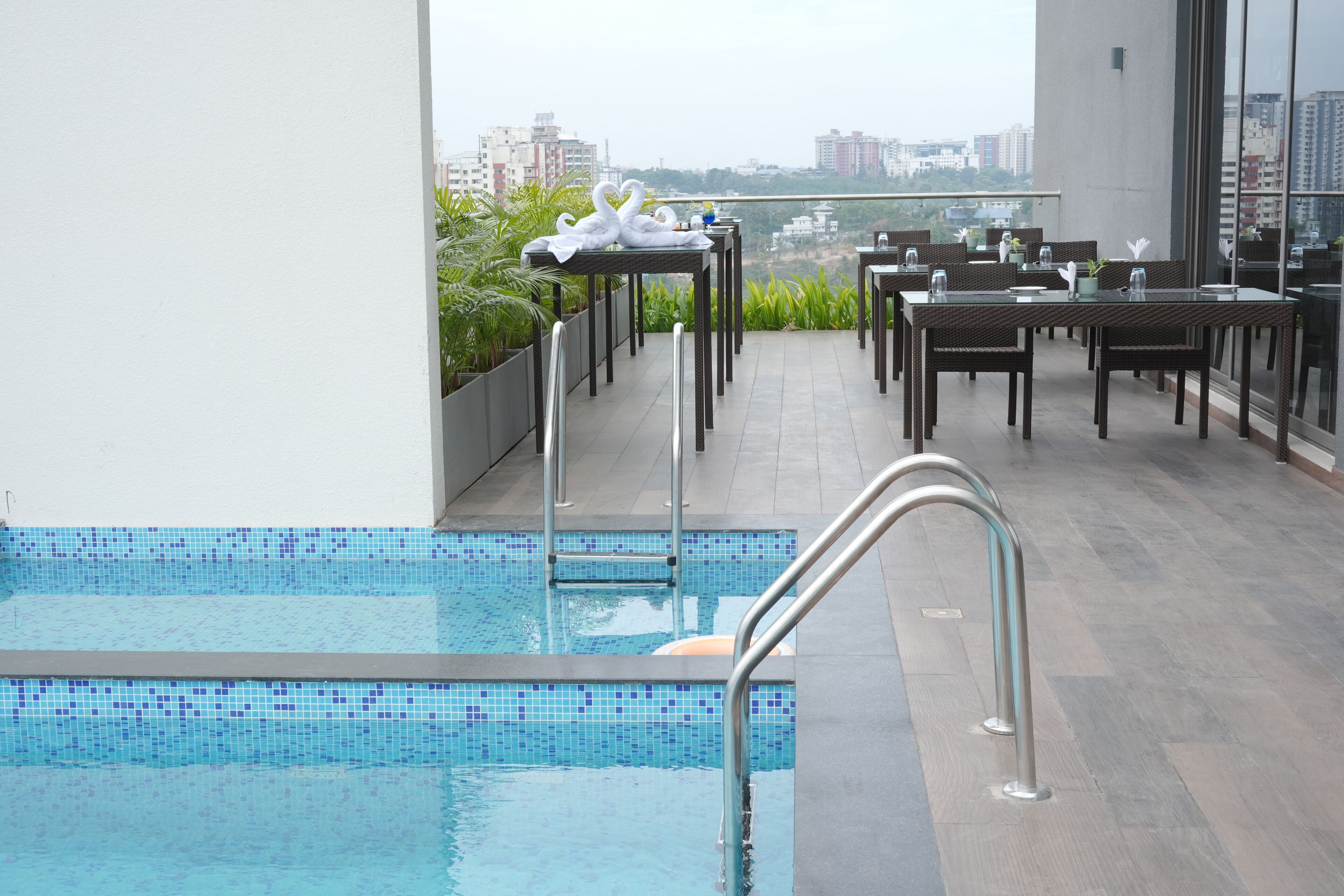 A rooftop pool area with a view of the city skyline, surrounded by dining tables and chairs.