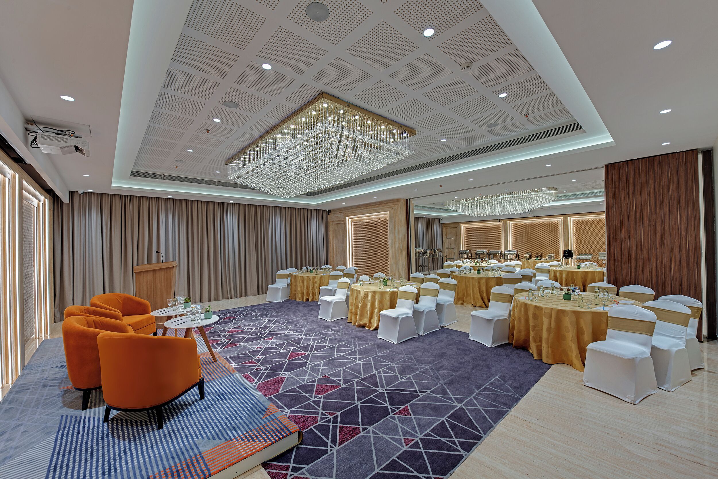 A conference room with round tables, white chairs, and a large chandelier.