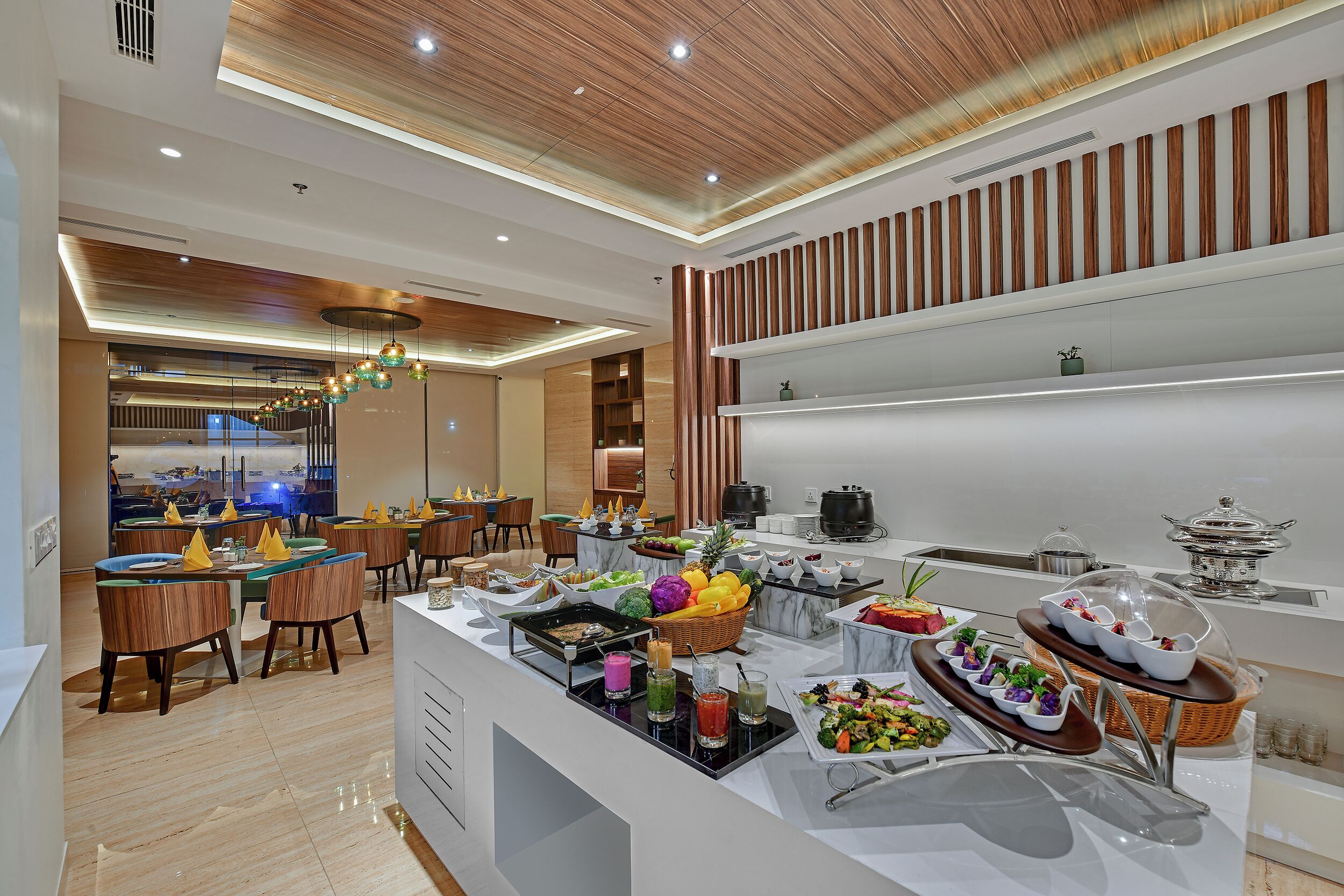 Zona ristoro di un hotel moderno con soffitto in legno, buffet con diverse pietanze e angolo salotto con tavoli e sedie.