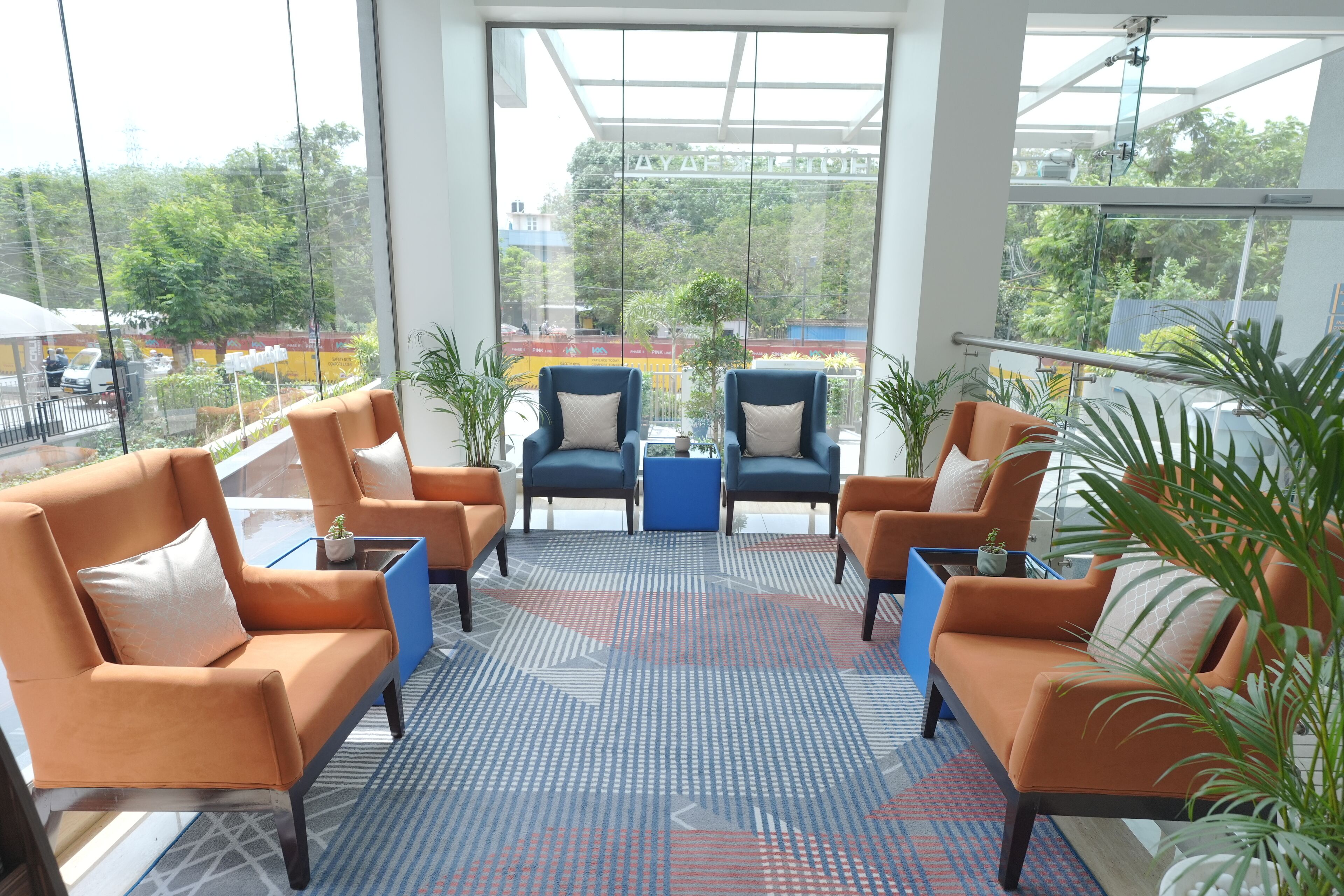 A modern indoor seating area with sofas and chairs, large windows with a view of the street, and a patterned floor.