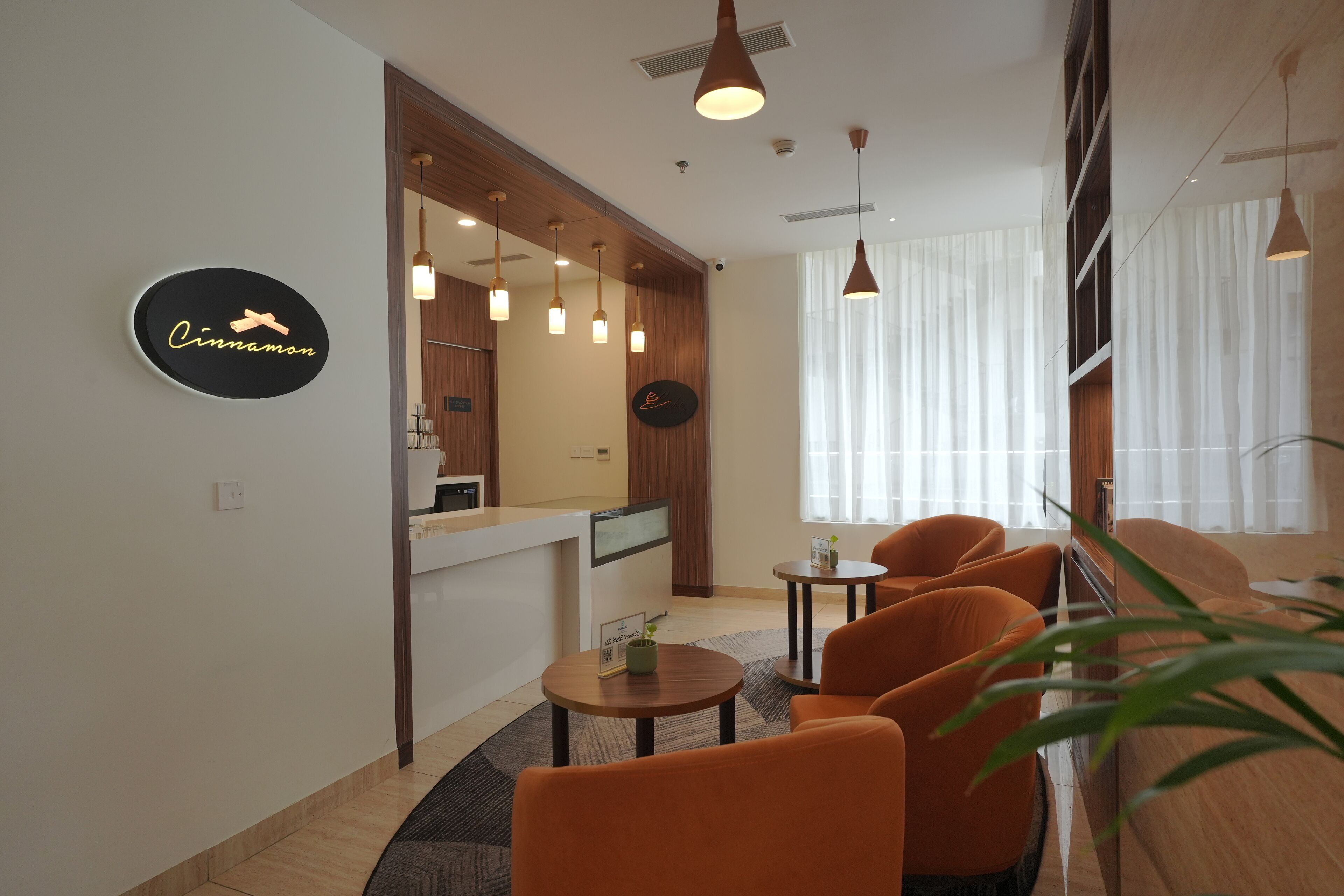 Un moderno vestíbulo de hotel con mostrador de recepción, asientos naranja, iluminación colgante y un letrero que dice "Cinnamon".