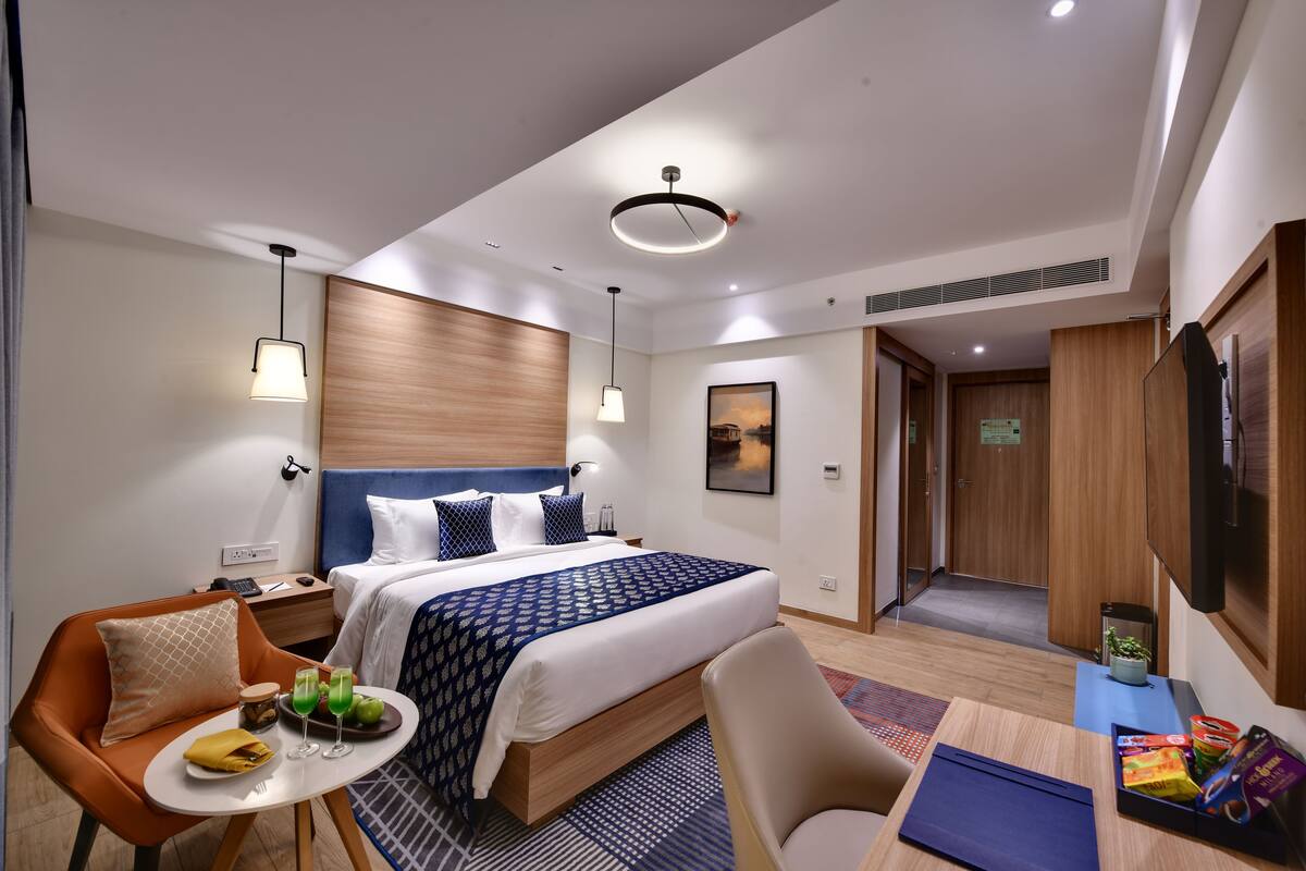 Een moderne hotelkamer met een groot bed, een bureau, een stoel, een klein tafeltje met een bord en drankjes, en een televisie aan de muur.