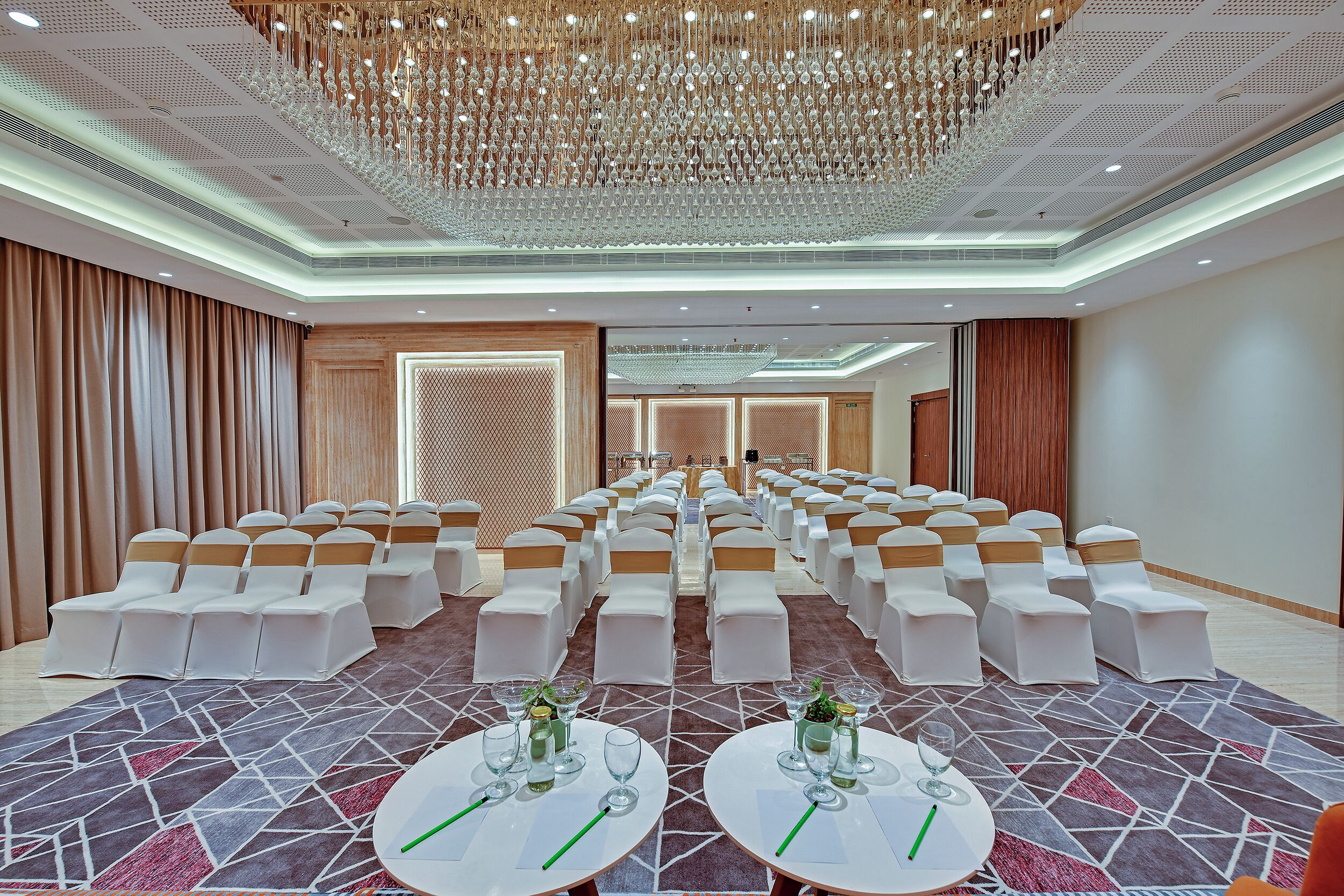 Una sala conferenze con file di sedie bianche, una moquette decorata e un grande lampadario.