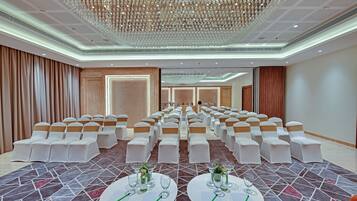 A conference room with rows of white chairs, a patterned carpet, and a large chandelier.