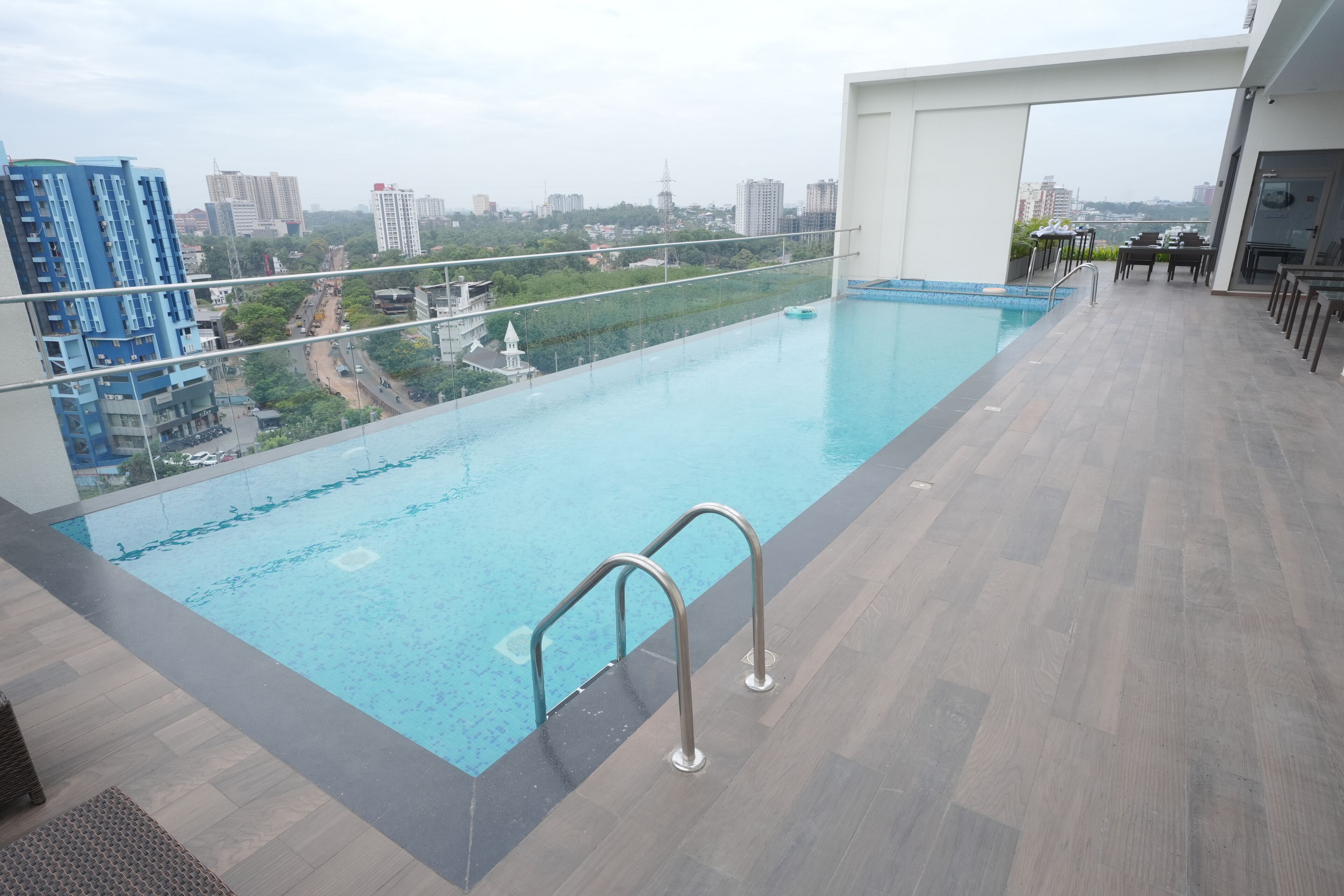 Una piscina infinita en la azotea con vista a la ciudad, un área de bar con asientos y un diseño arquitectónico moderno.
