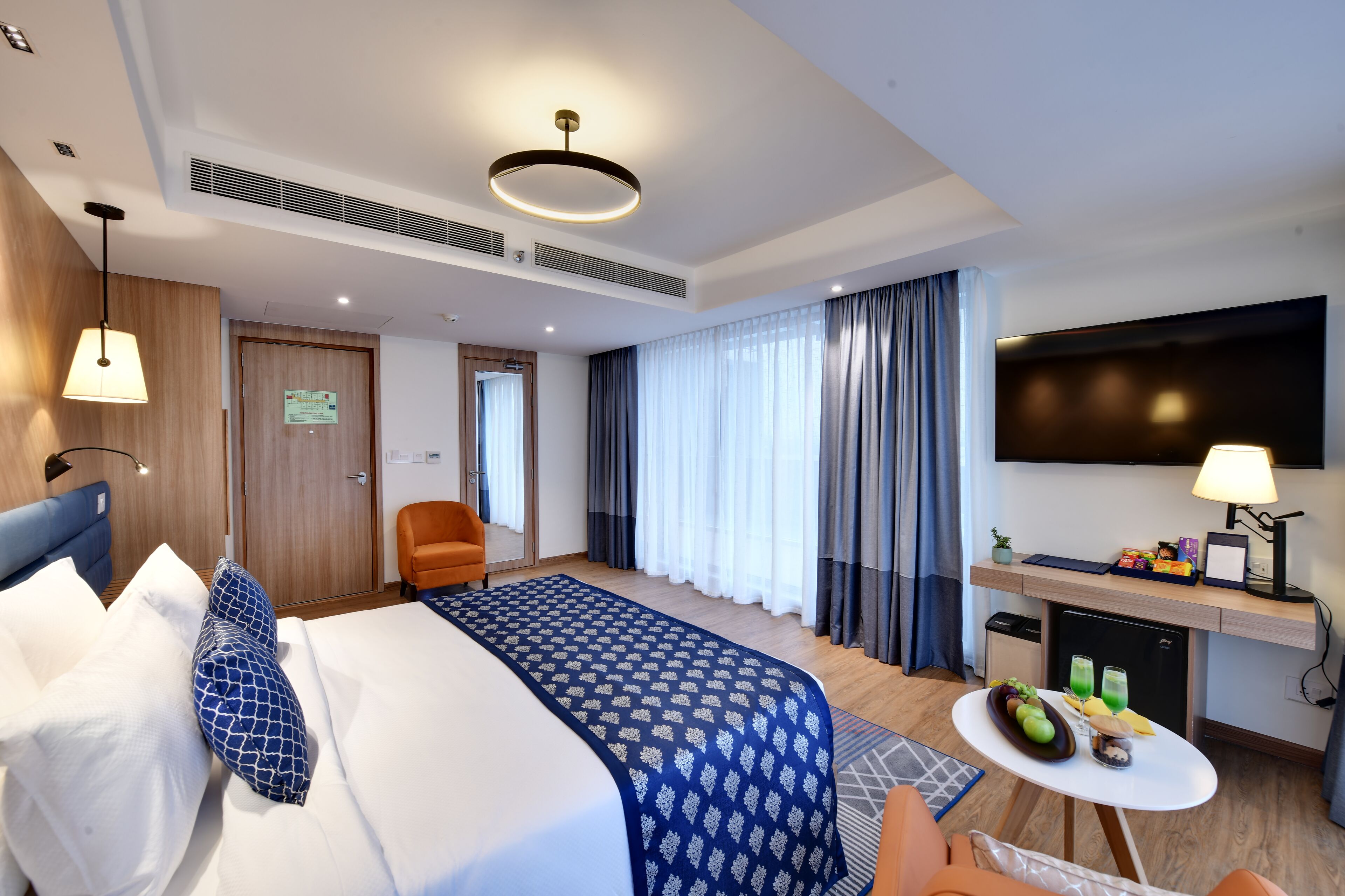 Habitación de hotel con una cama grande, un escritorio con televisor de pantalla plana, una pequeña mesa con fruta y una silla.