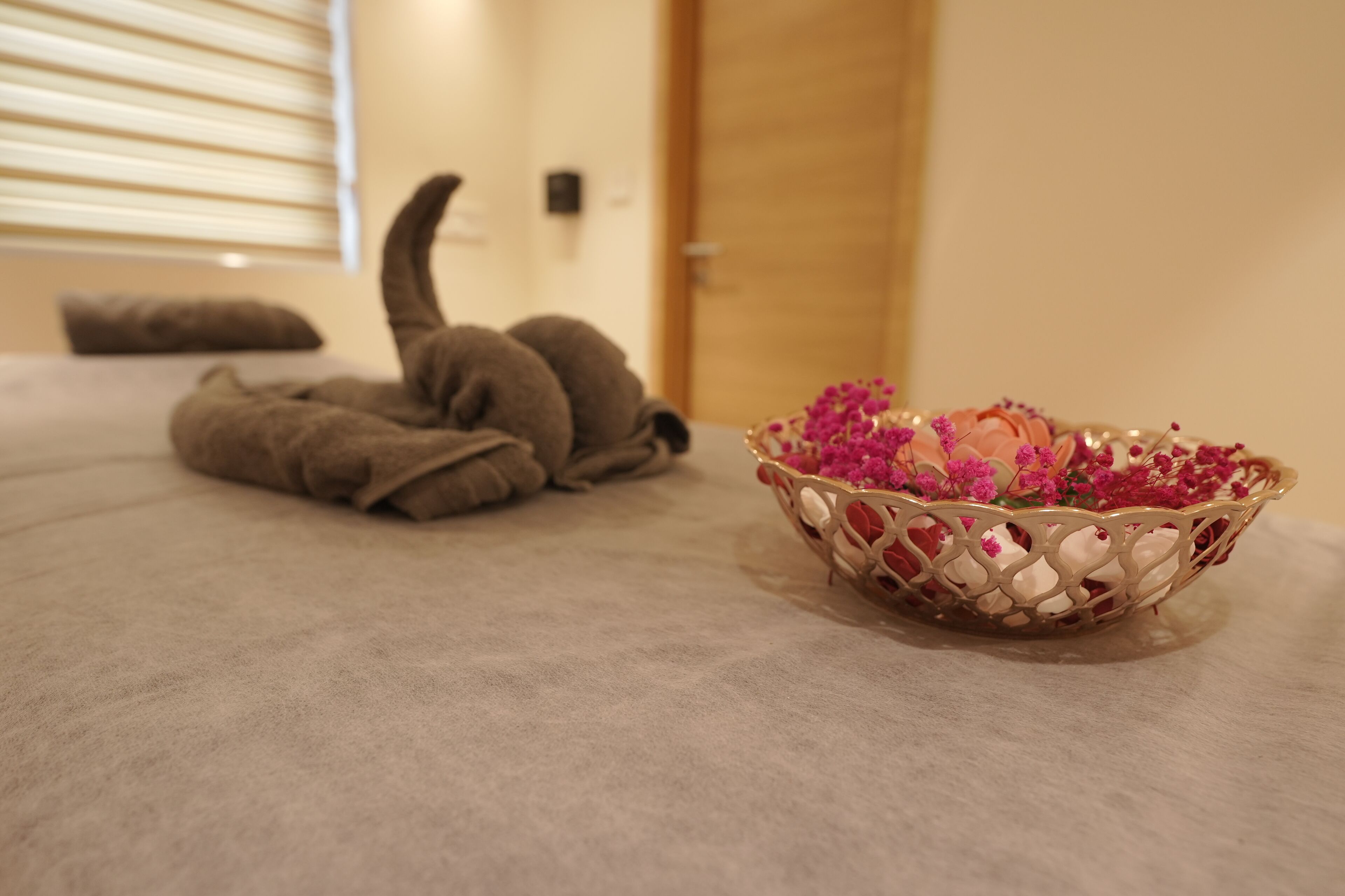 Een kamer met een bed, een decoratieve schaal met bloemen en een raam met zonwering.