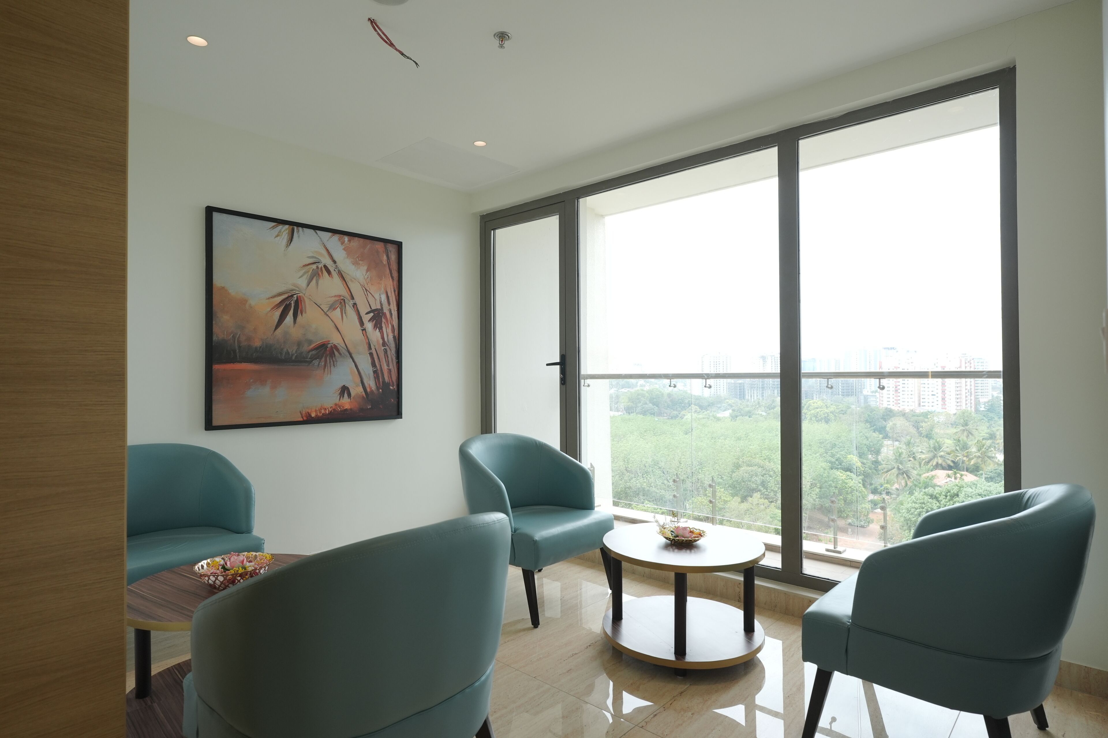 Un salon moderne avec des fauteuils turquoise, une table basse ronde et une grande fenêtre donnant sur la ville.