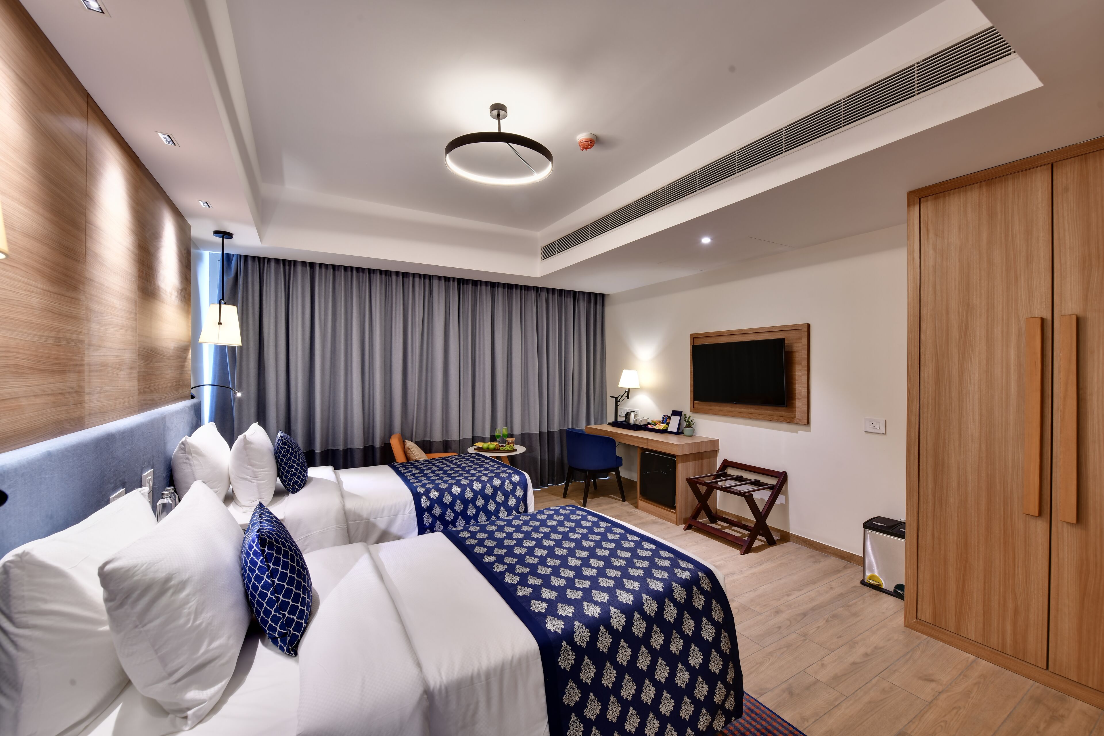Ein Hotelzimmer mit zwei Betten, einem Schreibtisch, einem Stuhl, einem Fernseher und einem Kleiderschrank.