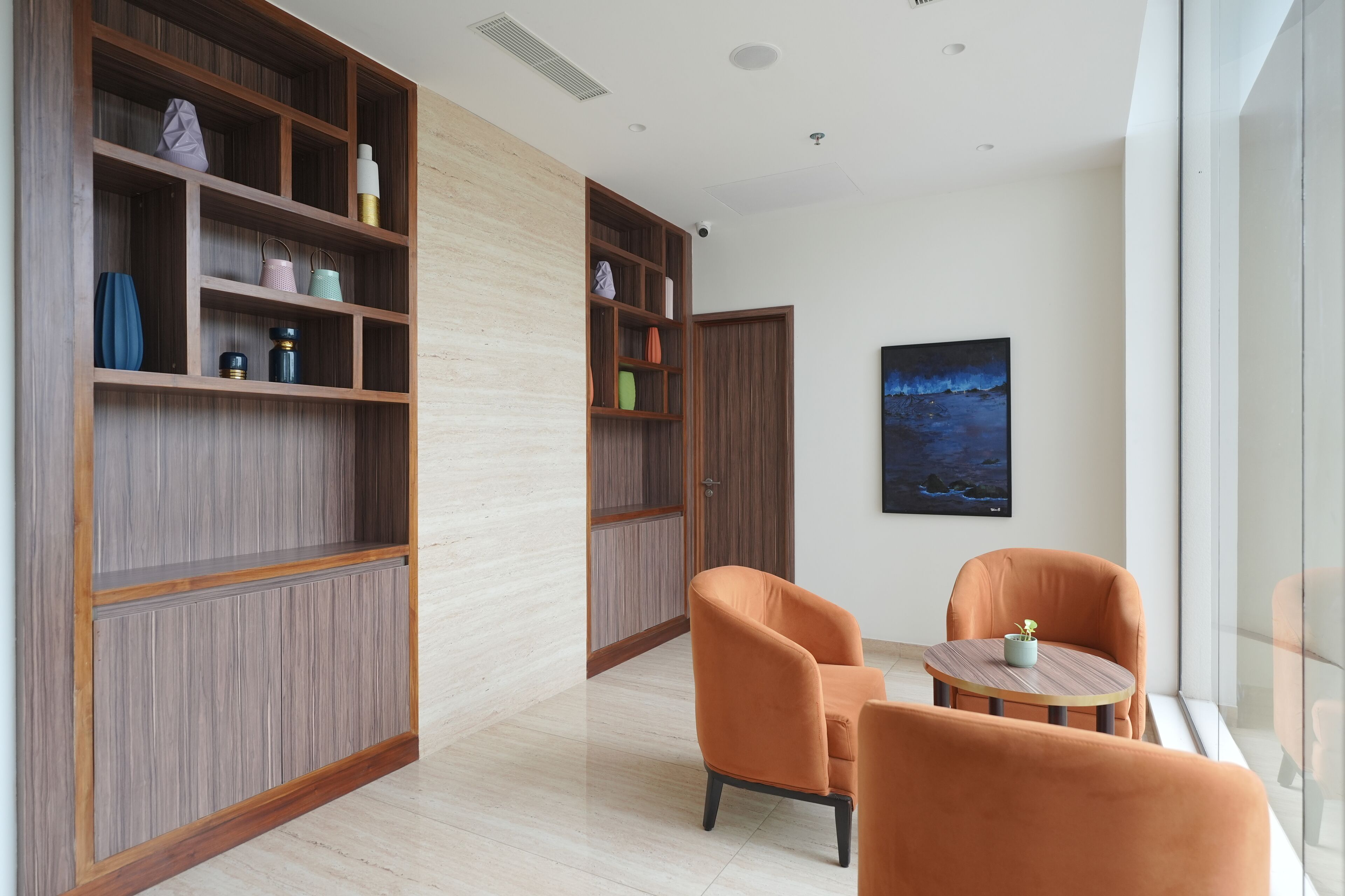 A modern room with wooden shelving, two orange chairs, a small table, and a painting on the wall.