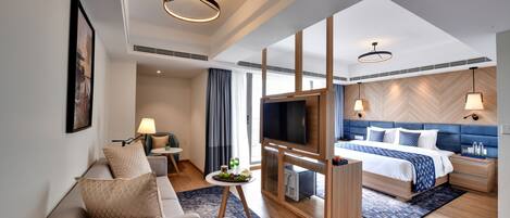 A modern hotel room with a sofa, TV, bed, and a small table with snacks.