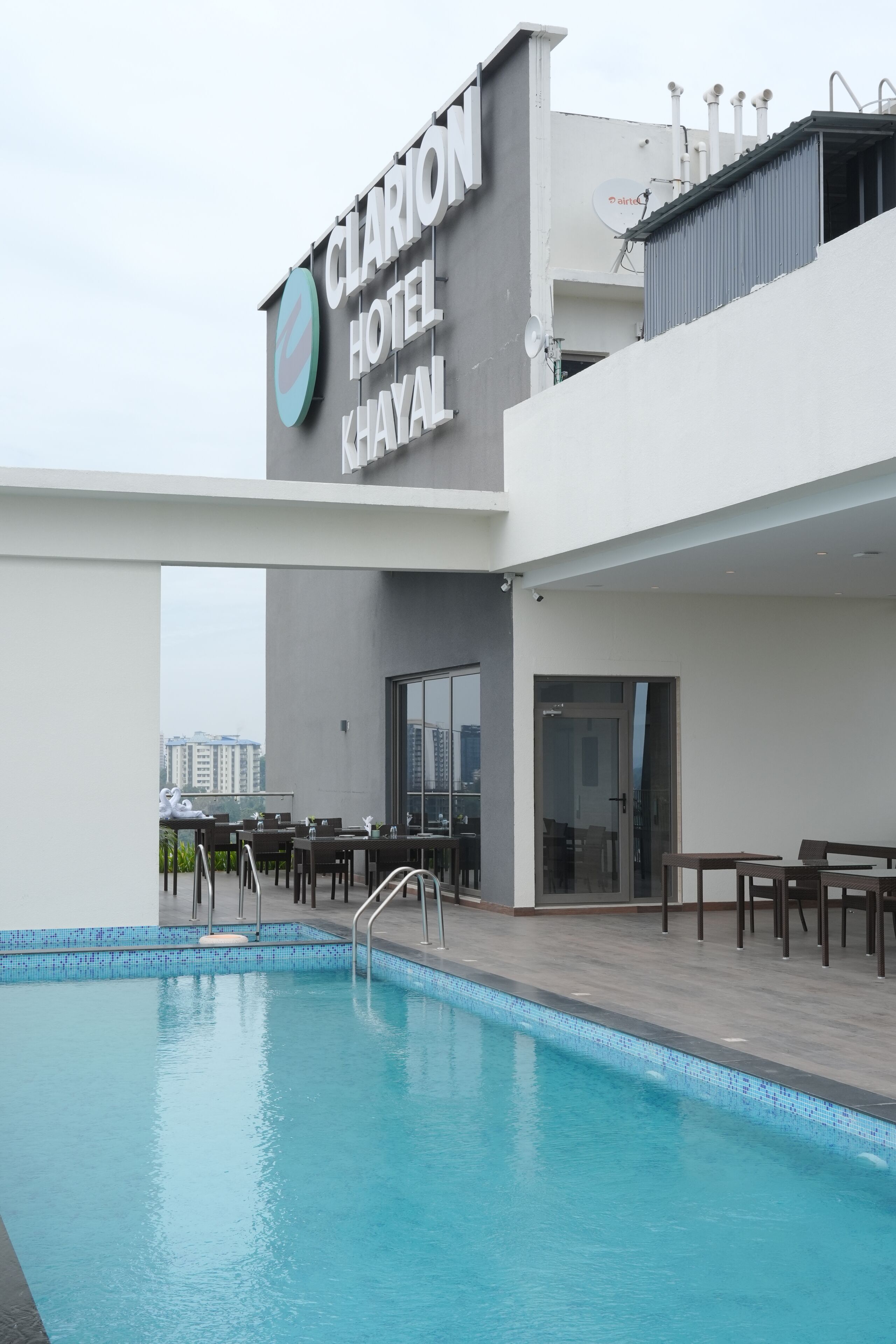 A hotel with a swimming pool, outdoor seating, and a view of the cityscape.