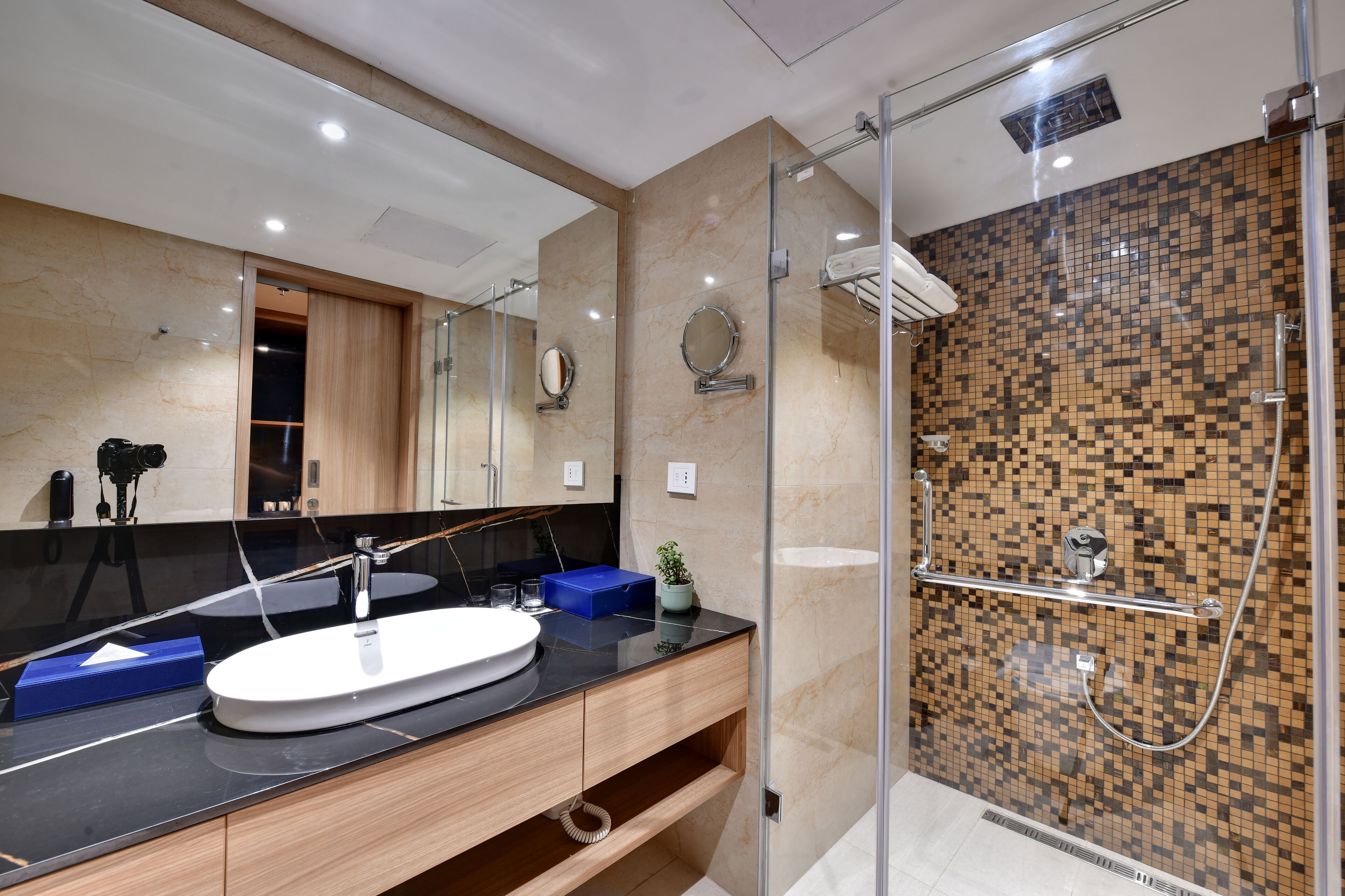 Een moderne badkamer met een grote spiegel, een ronde spiegel, een witte wastafel en een douchegedeelte met een mozaïek betegelde wand.