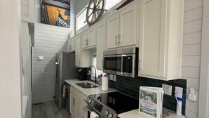 Een keuken met witte kasten, een roestvrijstalen fornuis, een magnetron en een grote wieldecoratie aan de muur.