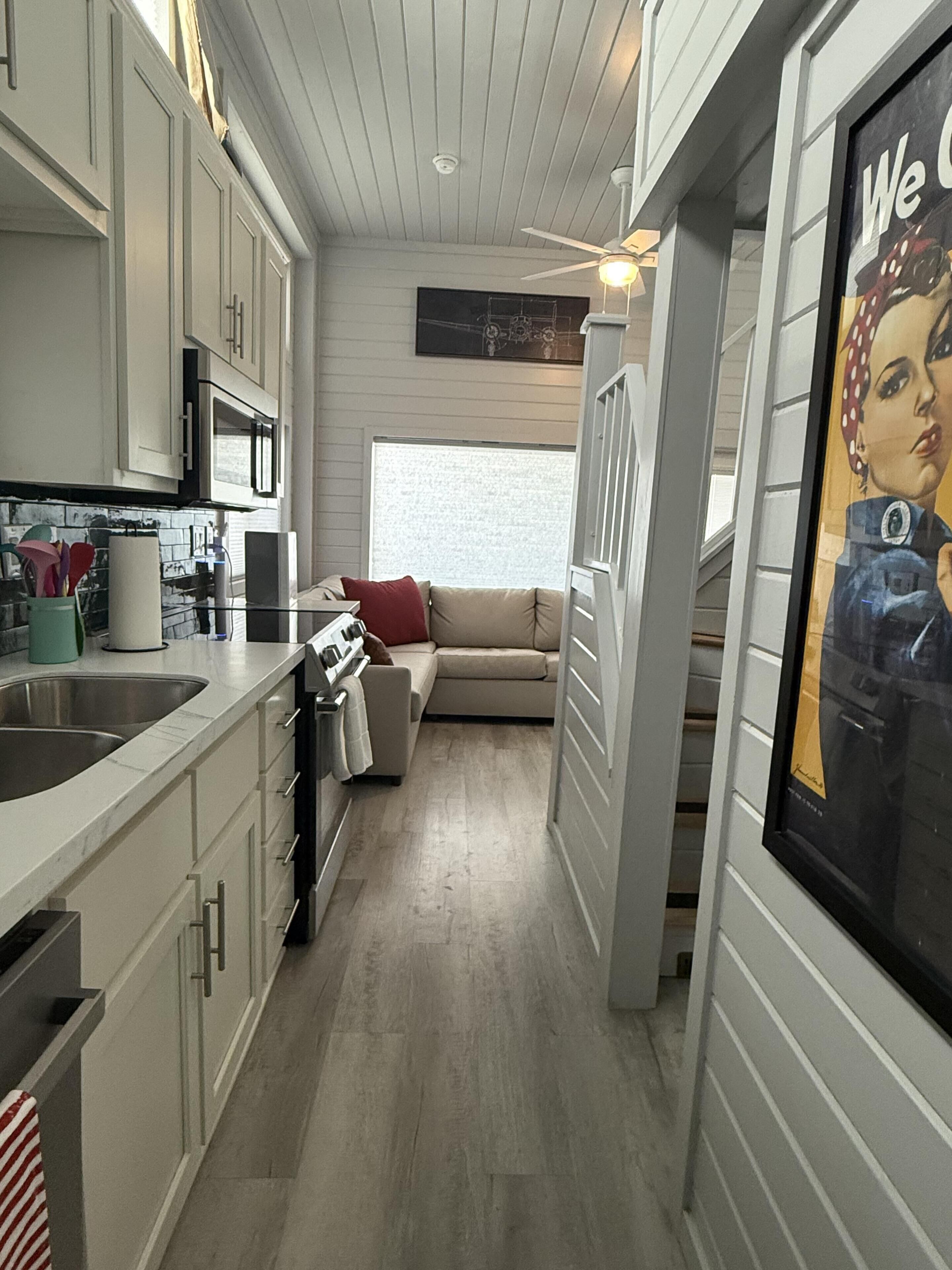 A narrow kitchen with a built-in oven, a dining area with a sofa, and a staircase leading to another level.