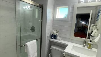 Een moderne badkamer met een glazen douchecabine, een wit toilet, een wastafel met spiegel erboven en een raam voor natuurlijk licht.
