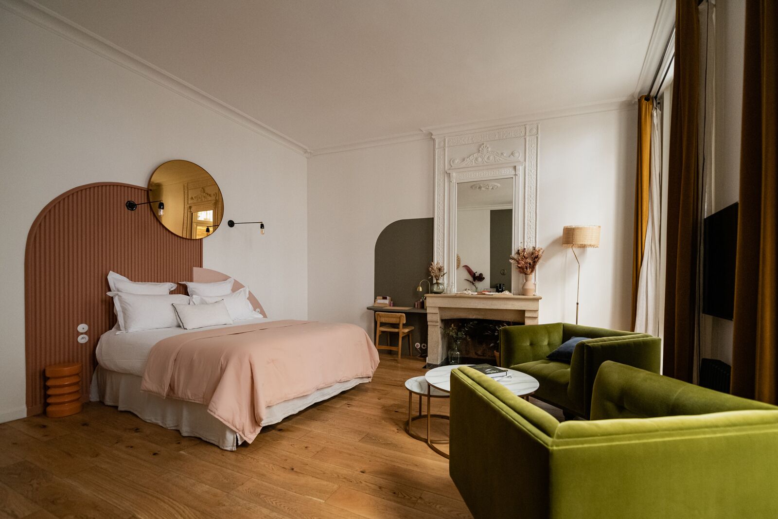 A modern hotel room with a bed, a desk, a green armchair, and a round mirror.