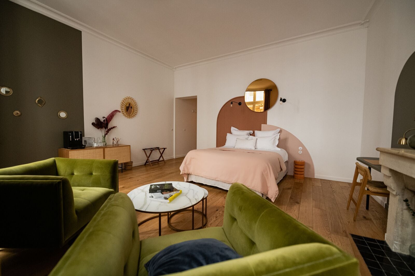 Un dormitorio moderno con una cama, sillones verdes, una mesita de centro y un pequeño escritorio.