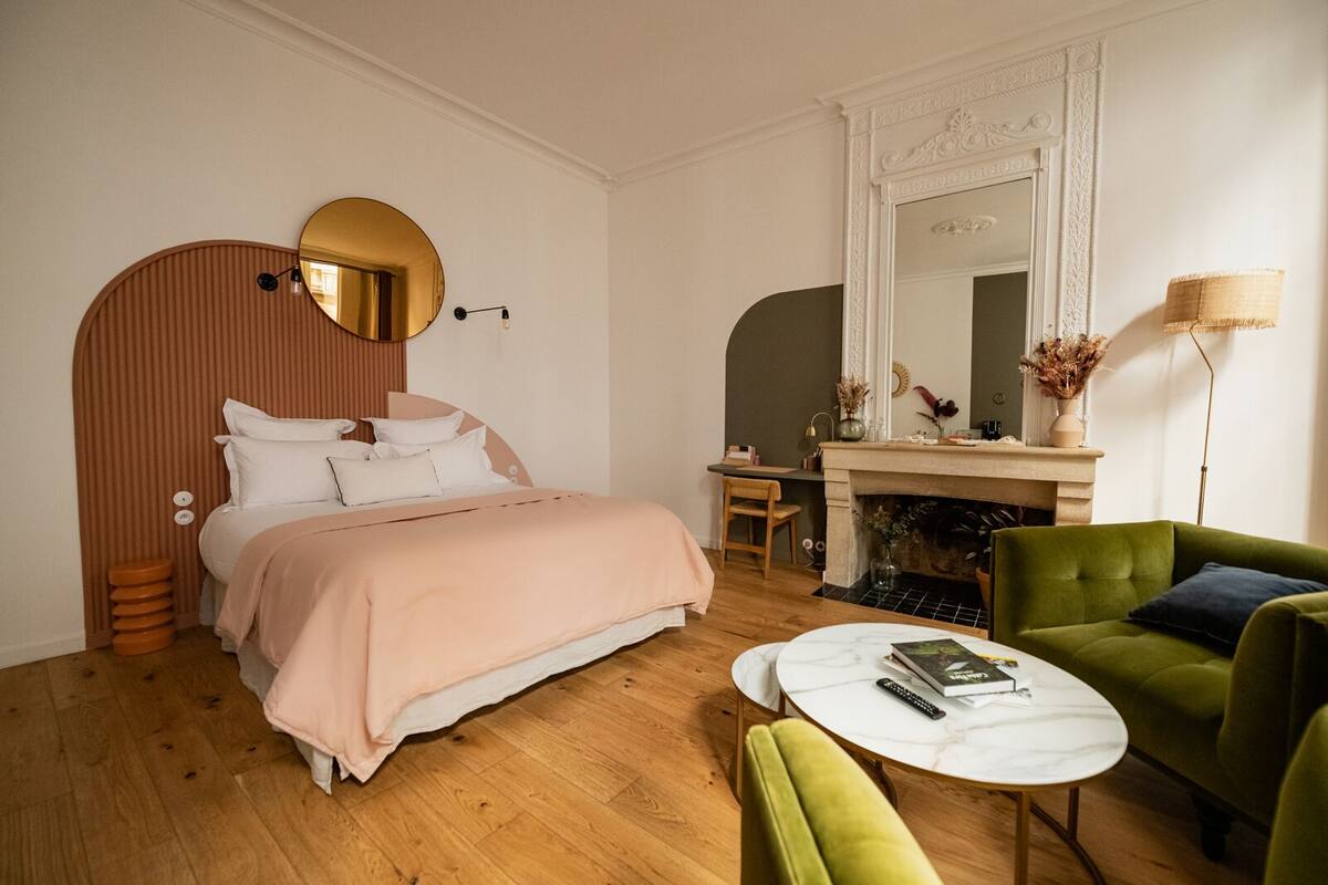 Quarto moderno com cama, poltrona verde, mesa de centro redonda e lareira.