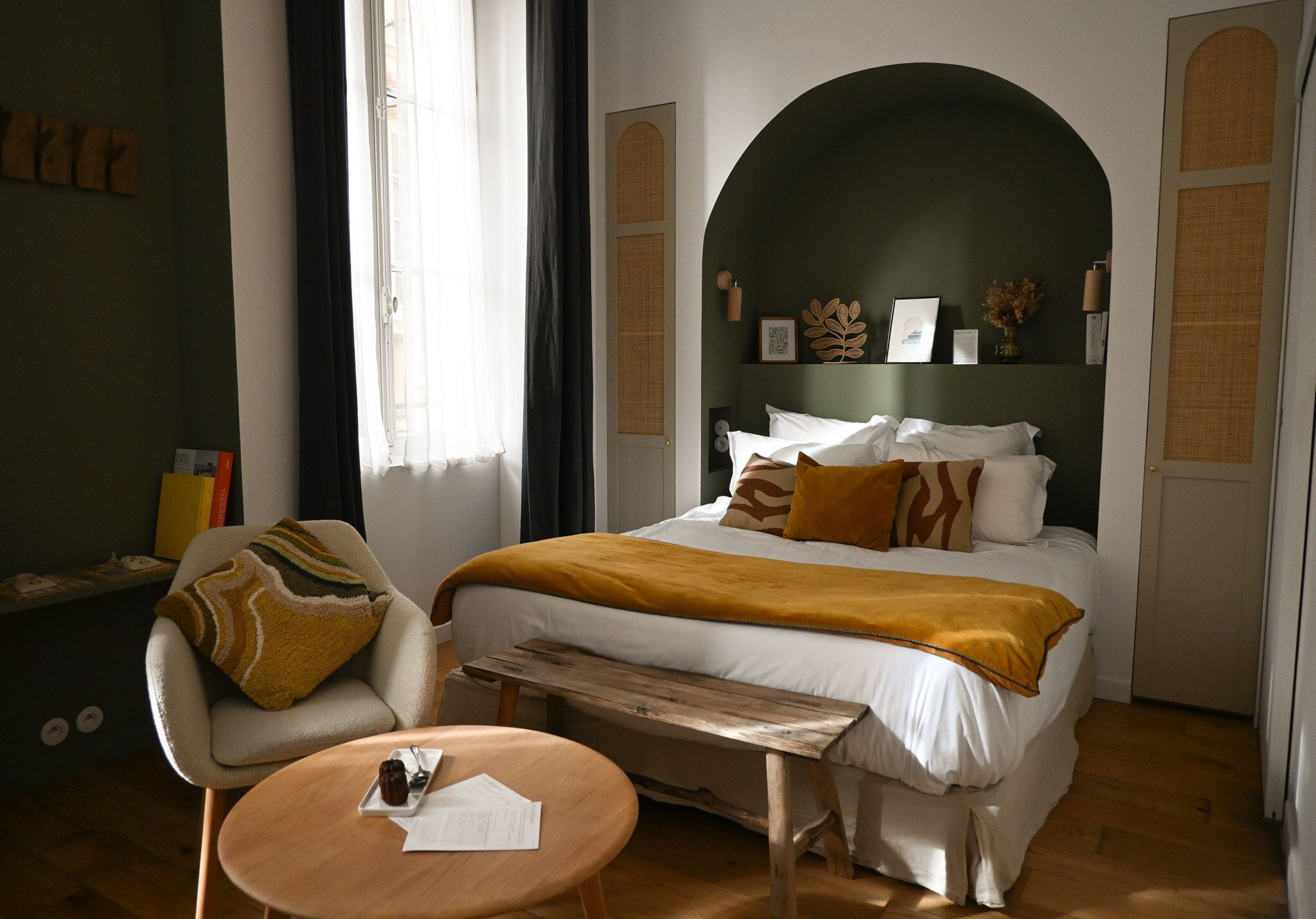 Habitació d'hotel amb llit, cadira, taula petita i finestra.