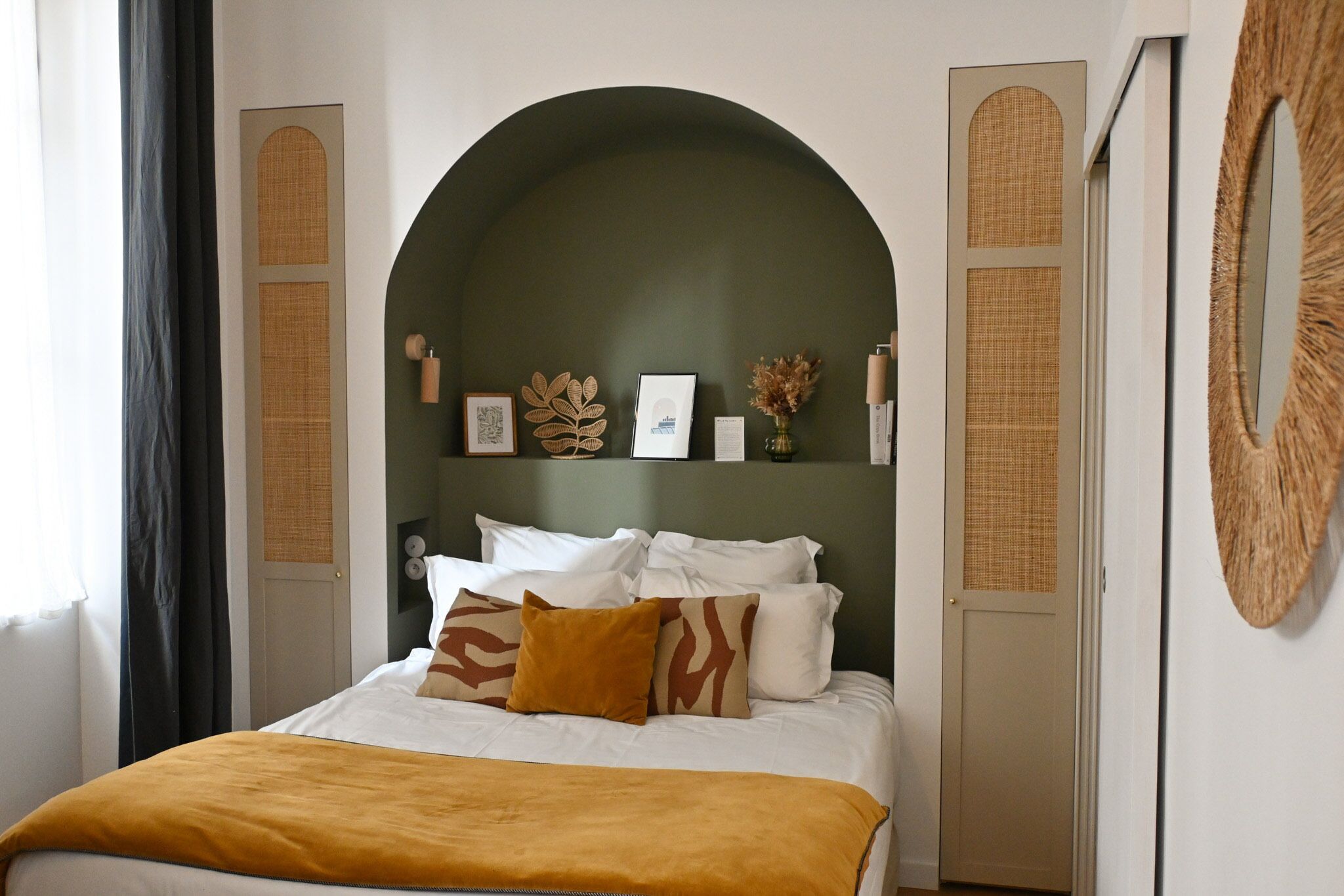 Une chambre à coucher avec un lit, une arche verte et un miroir.