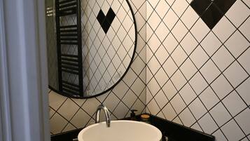 A bathroom with a round mirror, a white sink, and a black tiled wall with diamond patterns.