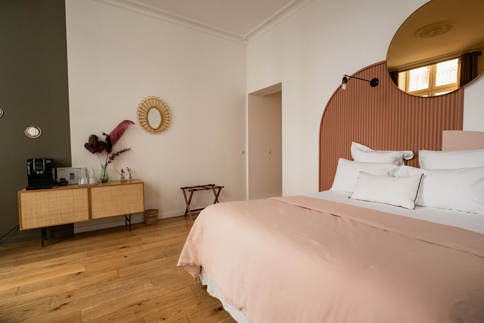 A bedroom with a bed, a wooden dresser, a mirror, and a wall-mounted light fixture.