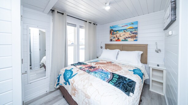 Une chambre à coucher avec un grand lit, une tête de lit en bois, un tableau représentant une scène de plage et une porte blanche.