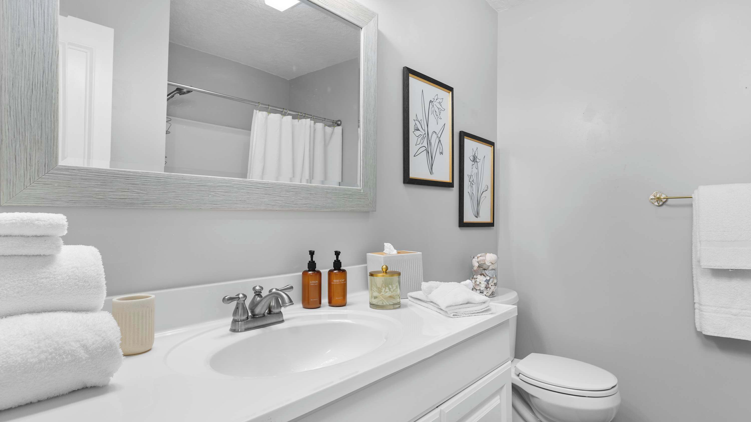 Un baño moderno con un lavamanos blanco, dos botellas de loción, una caja de pañuelos y un inodoro.