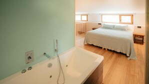 Een moderne slaapkamer met een groot, wit bad en een bed met een lichtkleurige dekbedovertrek, en een houten vloer.