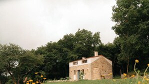 Een stenen huis met een schuin dak, omgeven door een grasveld en bomen.