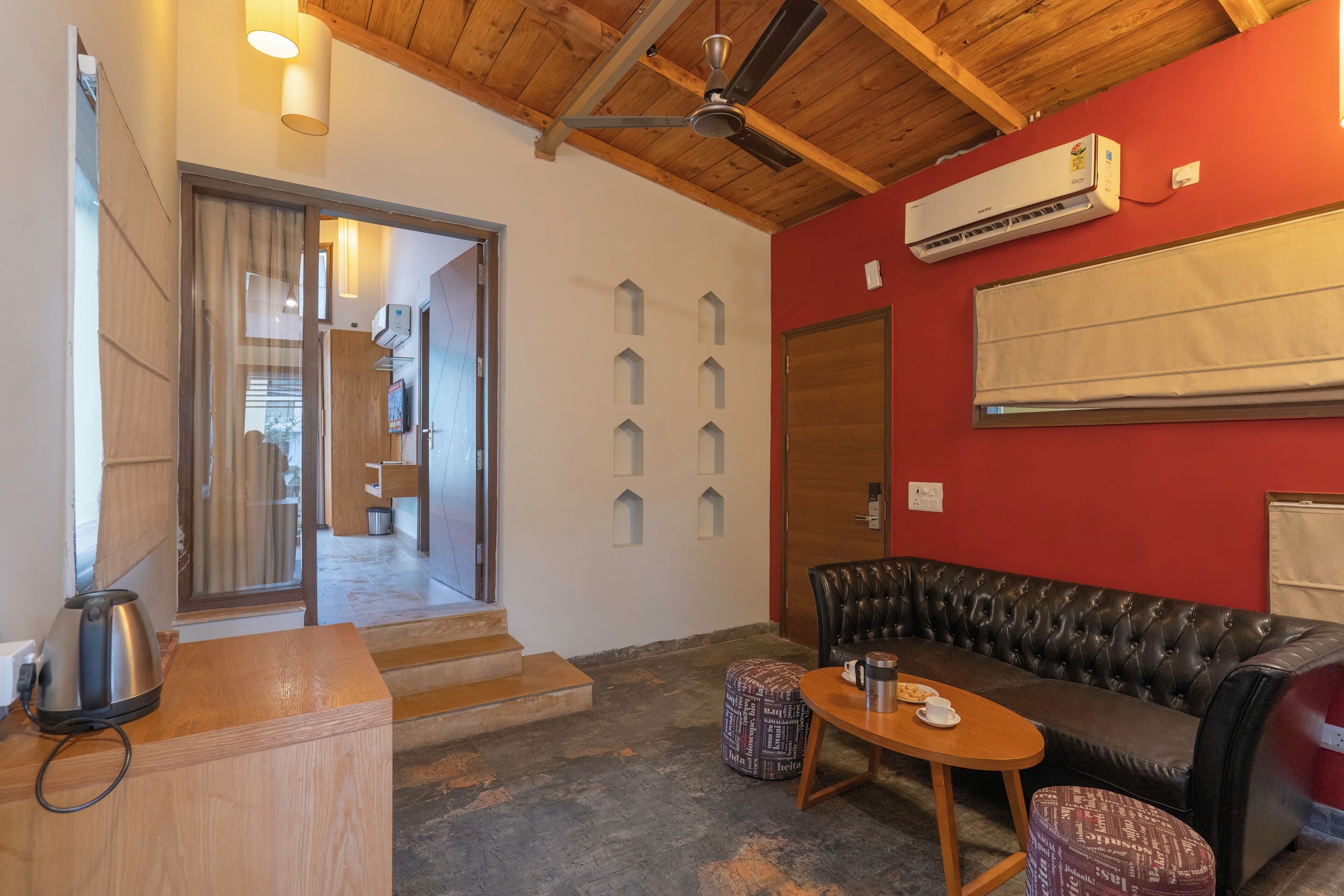 A cozy room with a wooden ceiling, a black leather sofa, a small wooden table, and a red accent wall.