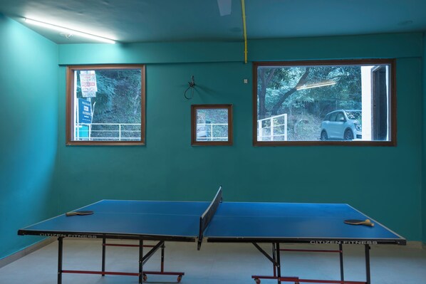 Une table de ping-pong dans une pièce aux murs de couleur turquoise et aux grandes fenêtres.