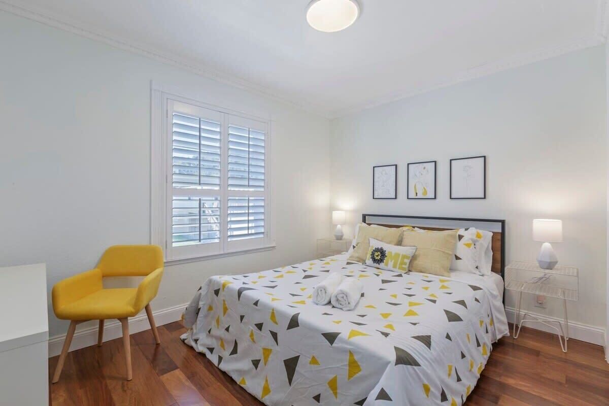 A bedroom with a bed, a chair, a window with blinds, and wall-mounted lights.