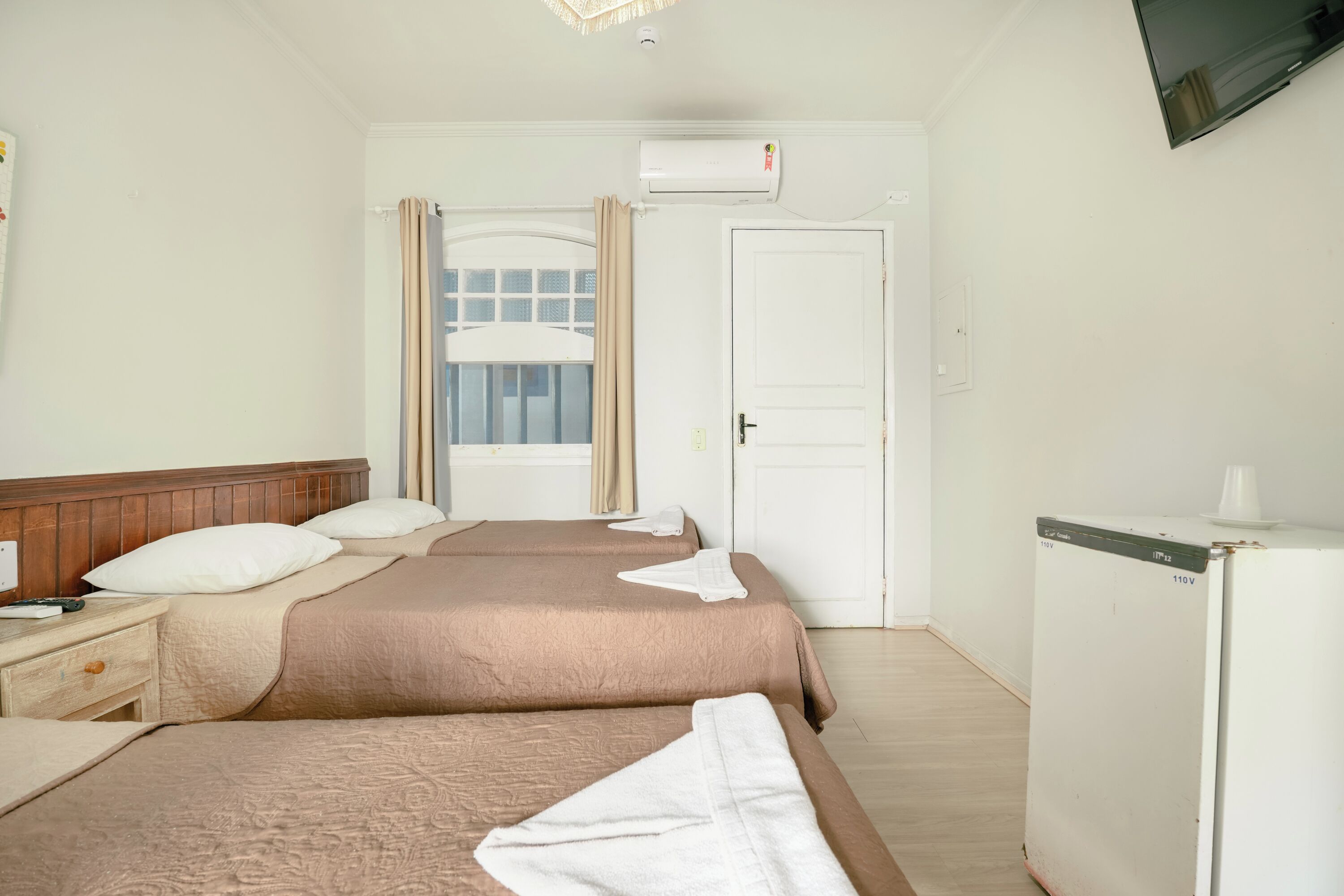 Habitación de hotel con dos camas, televisión, aire acondicionado y refrigerador.