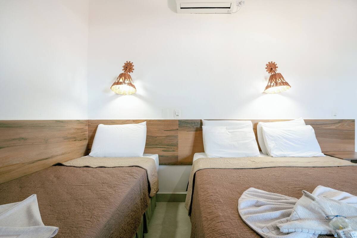 Habitación de hotel con dos camas, cada una con cabecero de madera, ropa de cama blanca y una lámpara de pared.