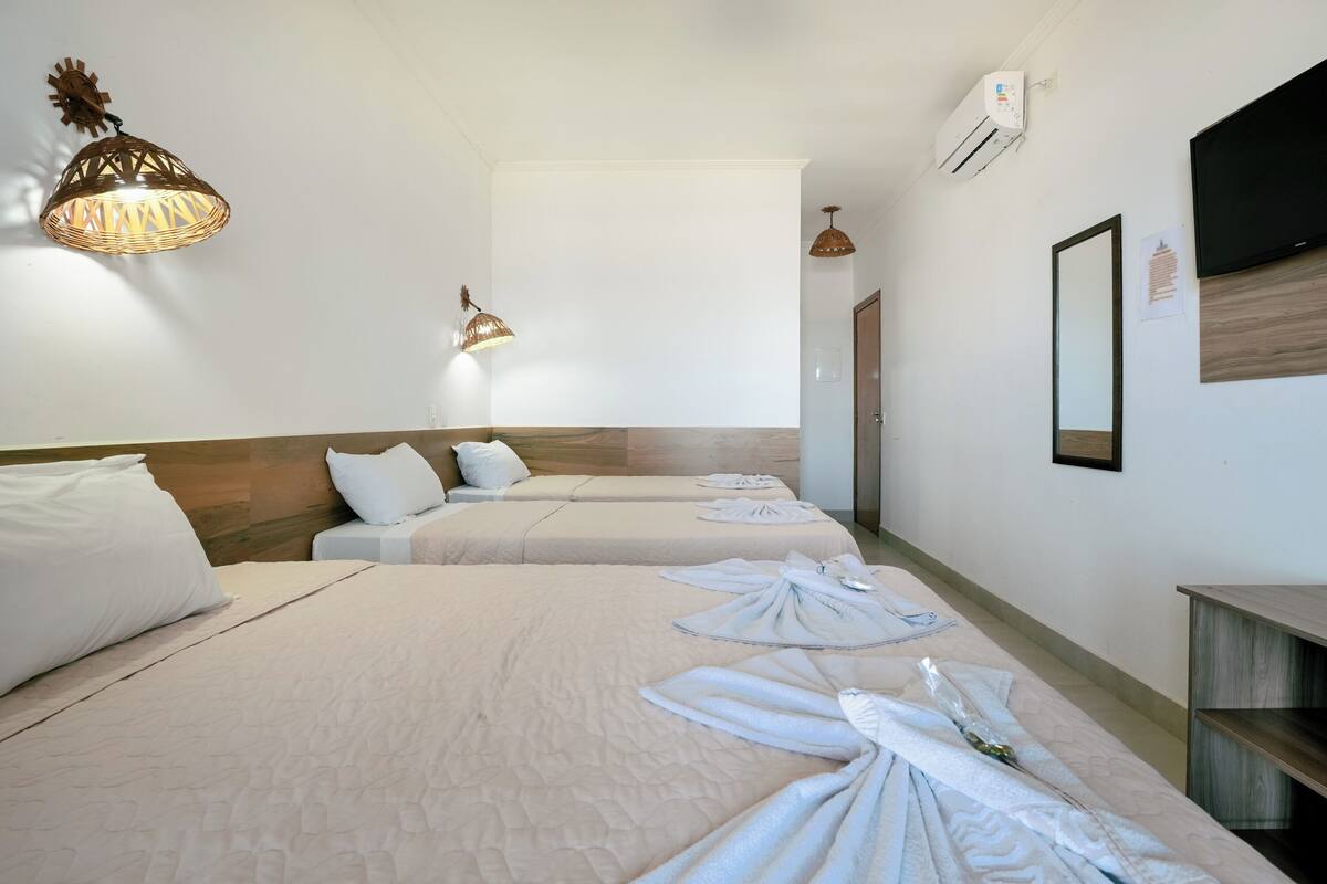 Habitación de hotel con dos camas, un ventanal grande, un televisor montado en la pared y un ventilador de techo.
