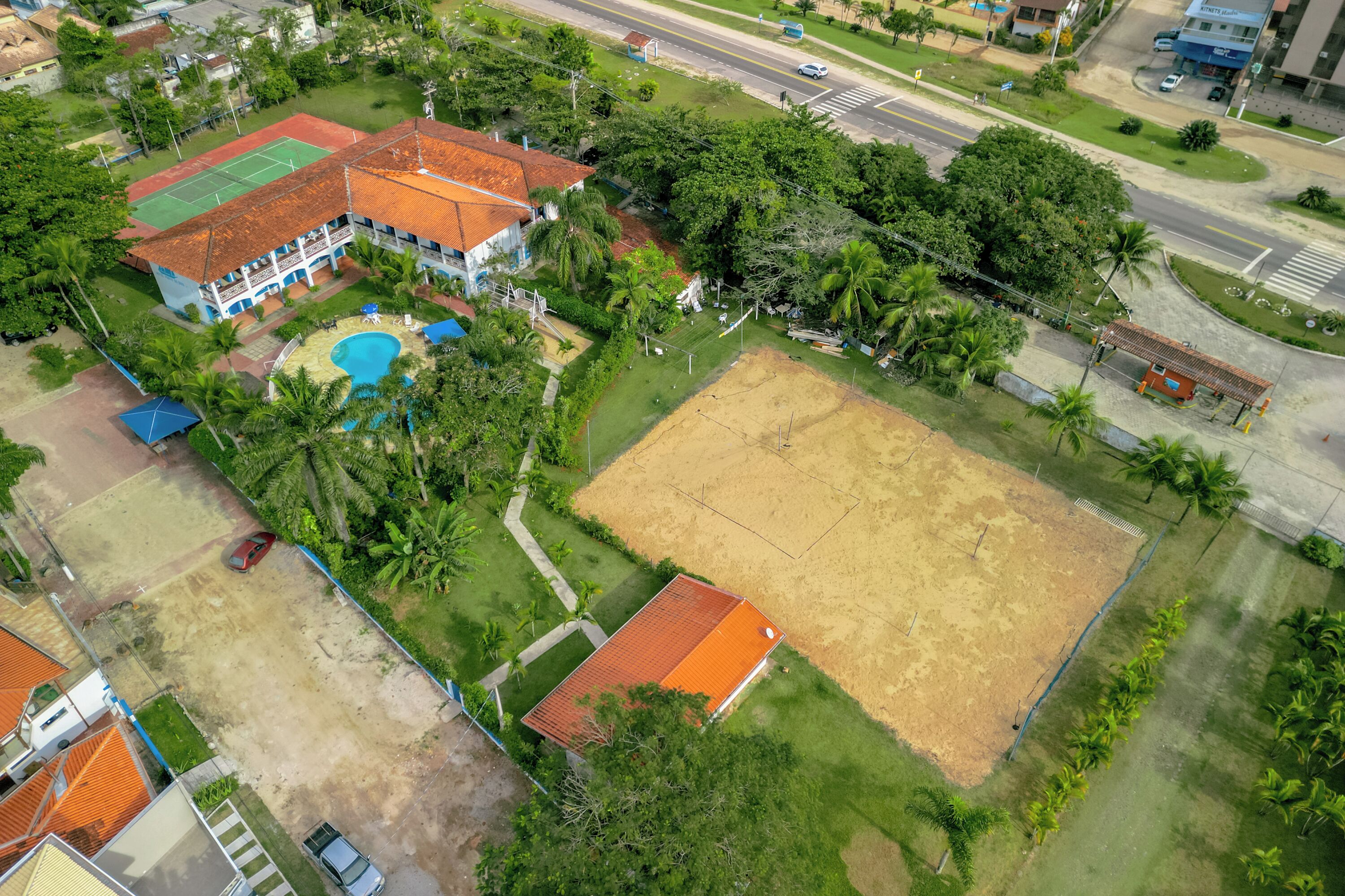 Eine Luftaufnahme einer Wohngegend mit einem großen Haus, das einen Swimmingpool, einen Tennisplatz und einen umzäunten Garten hat.