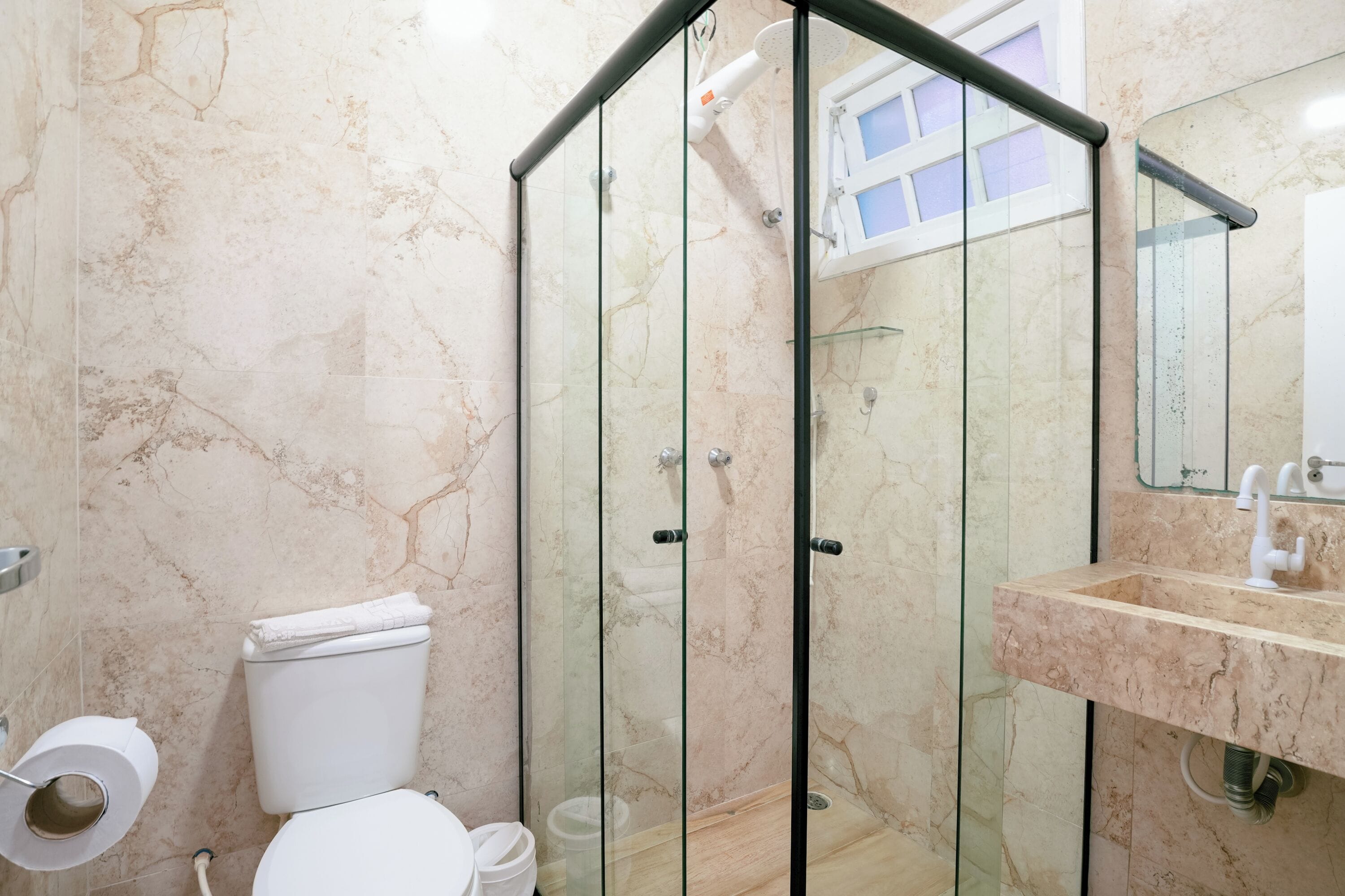 A modern bathroom with a glass-enclosed shower, a toilet, and a sink with a marble countertop.