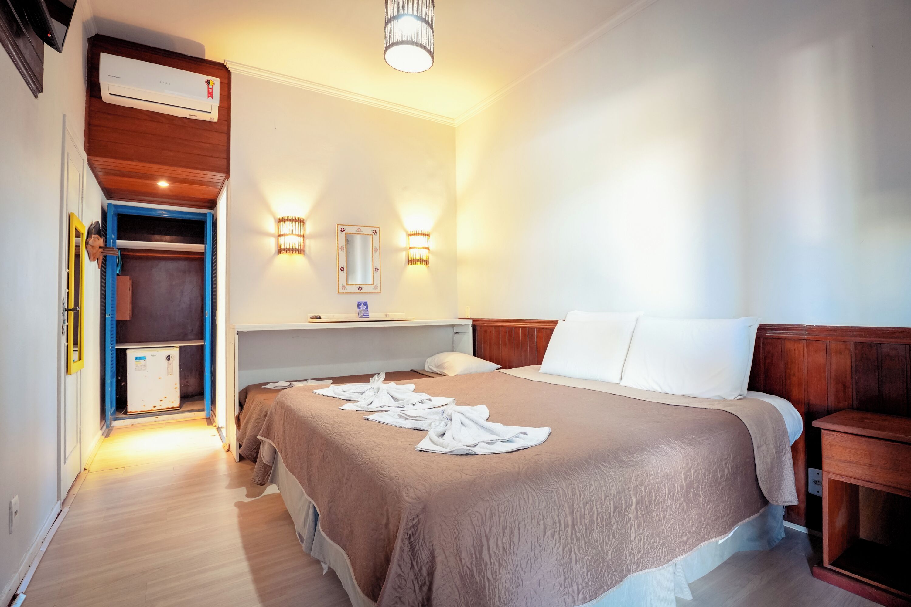 Una habitación de hotel con cama, mesita de noche, armario y equipo de aire acondicionado.