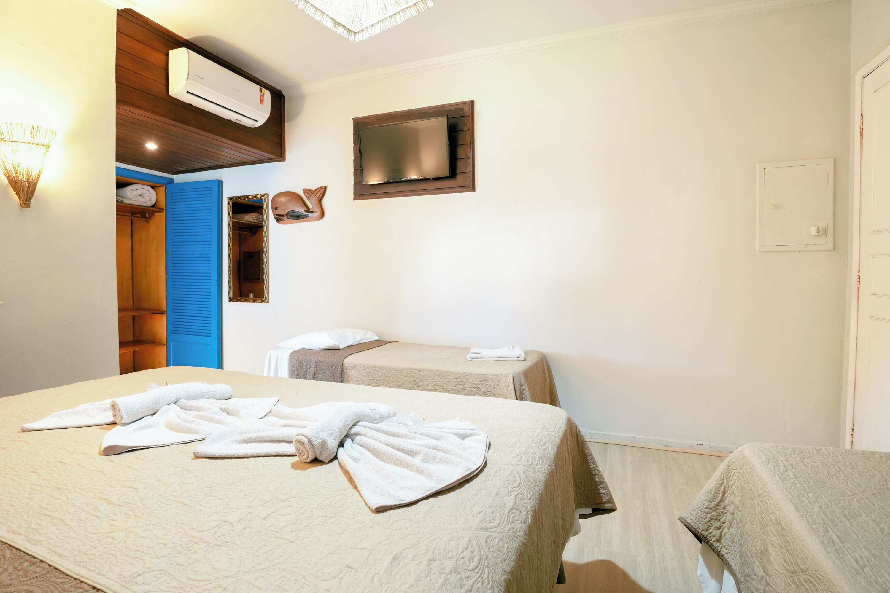 A hotel room with two beds, a TV mounted on the wall, an air conditioning unit, and a wooden door.