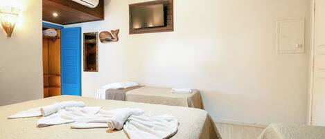 A hotel room with two beds, a TV mounted on the wall, an air conditioning unit, and a wooden door.