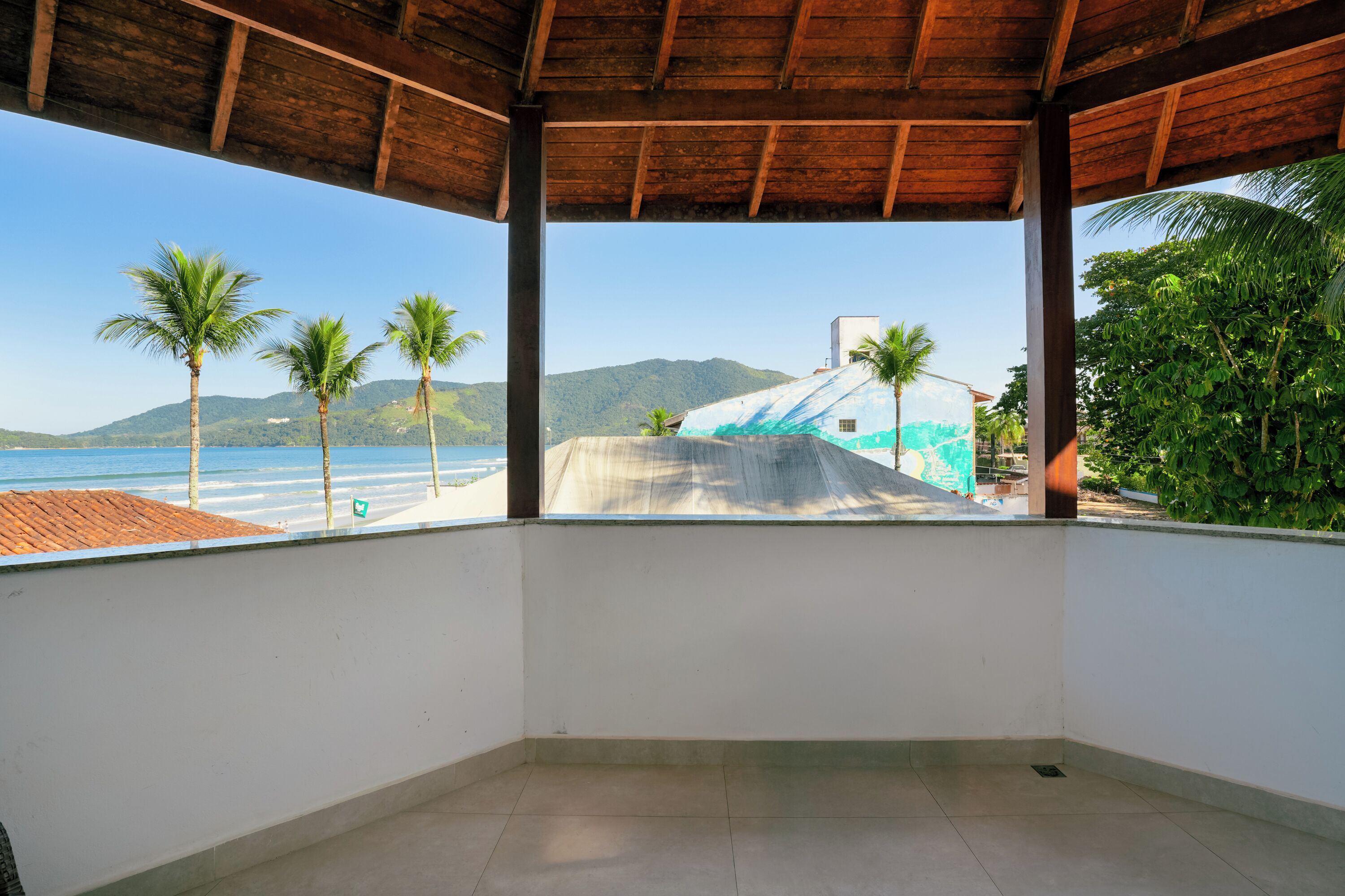A covered balcony with a view of the beach and mountains.