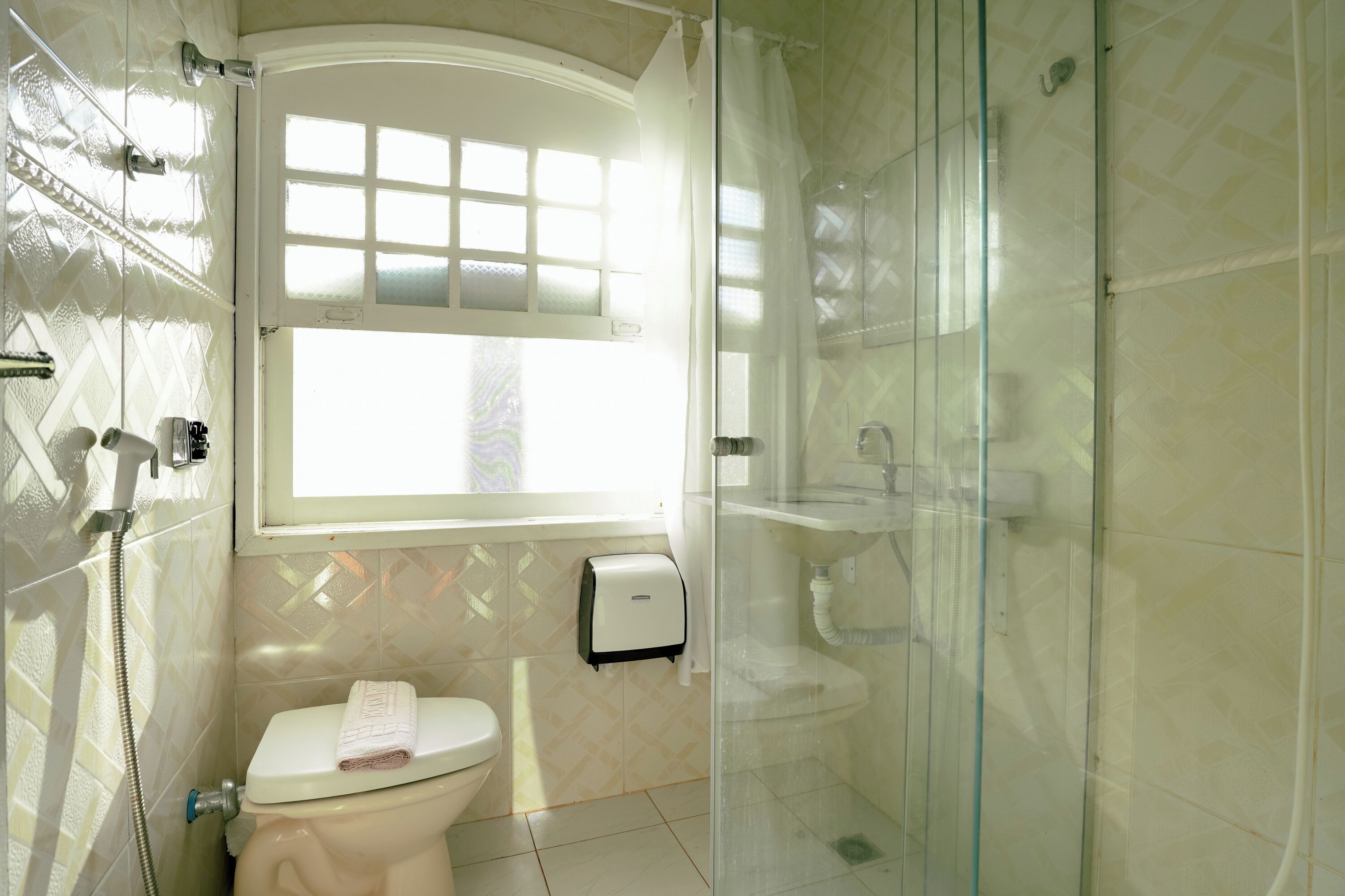 Un baño con inodoro, ducha con mampara de vidrio y ventana.